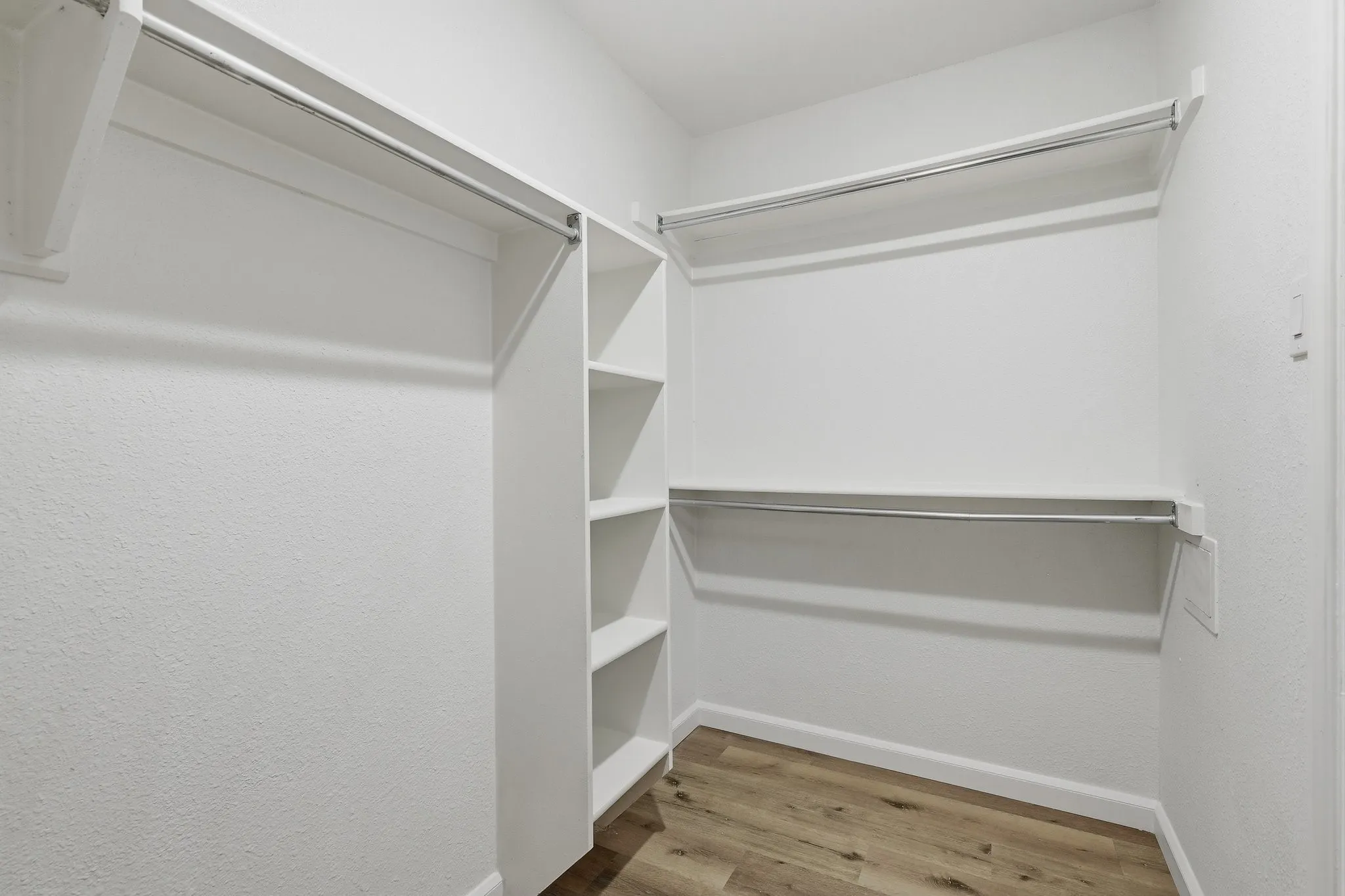 Walk-in closet featuring built-in shelving, two levels of hanging rods, and wood-finish flooring