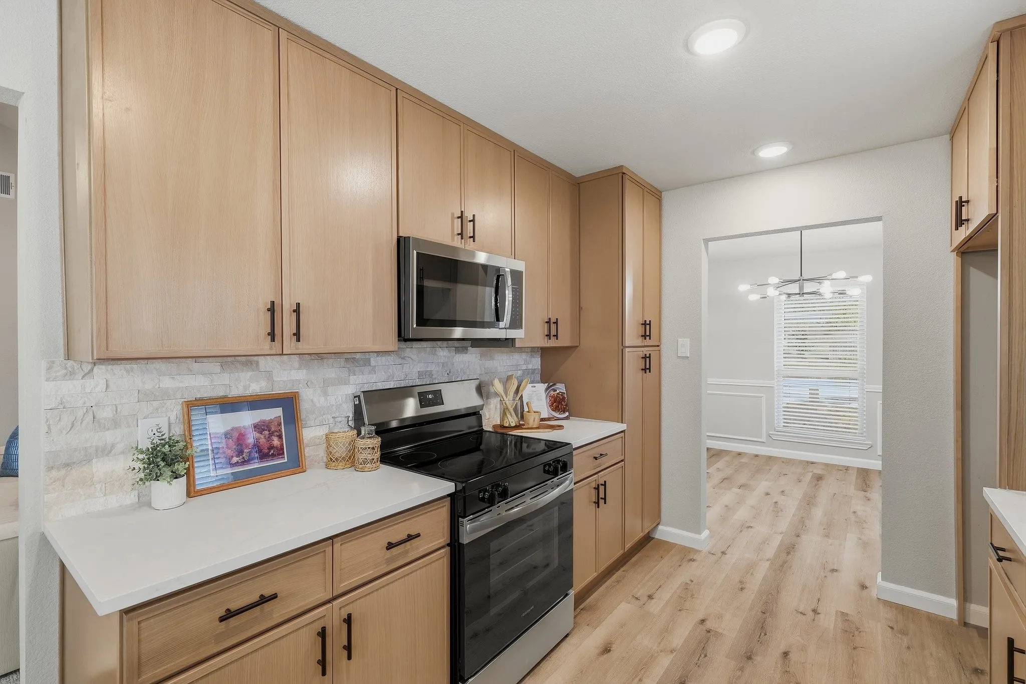 Kitchen featuring light wood-finish cabinetry with dark hardware, white countertops, stacked stone-look backsplash, and stainless steel appliances