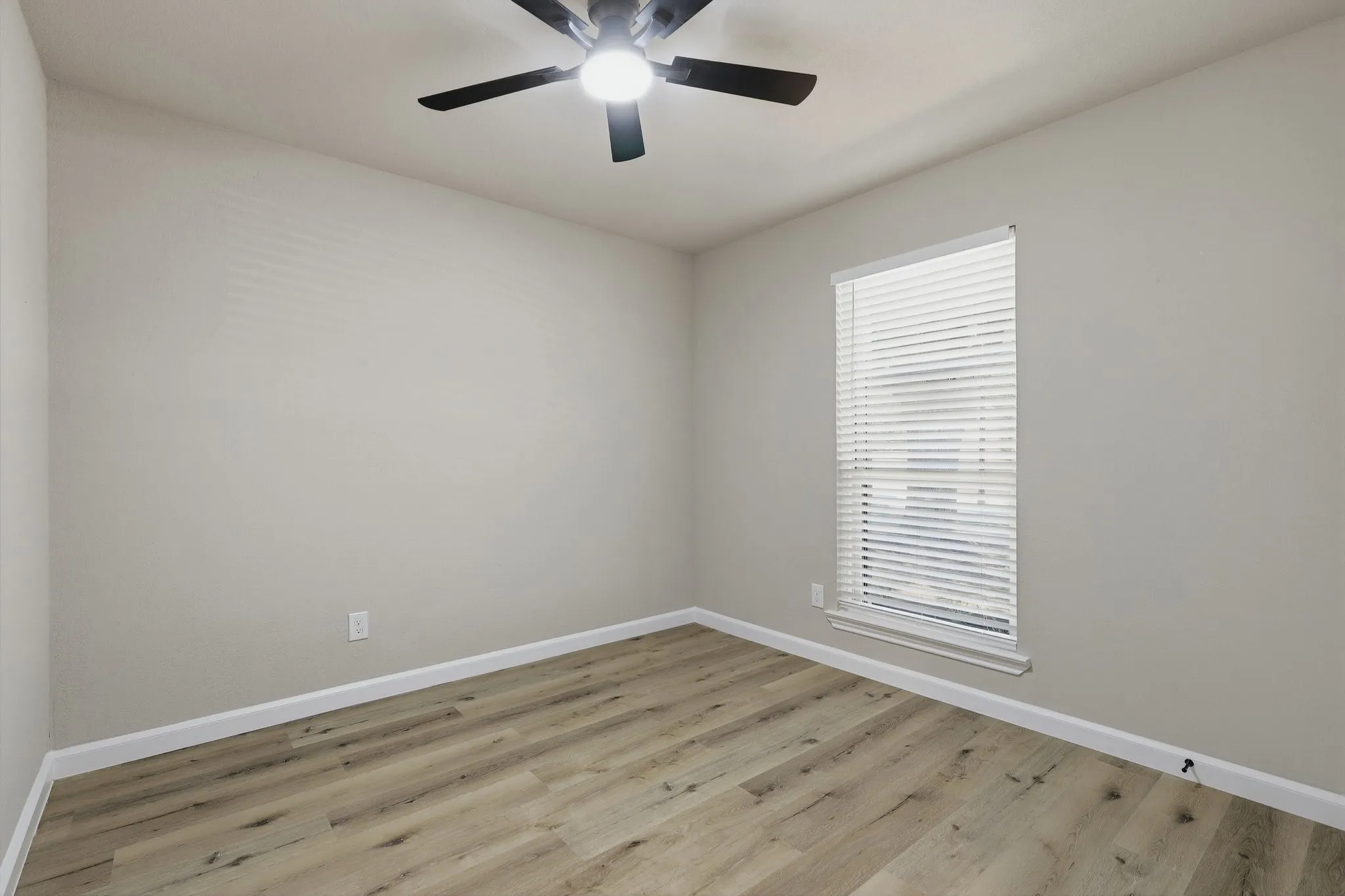 Neutral wall paint, wood-finish flooring, ceiling fan with integrated lighting, and window with blinds