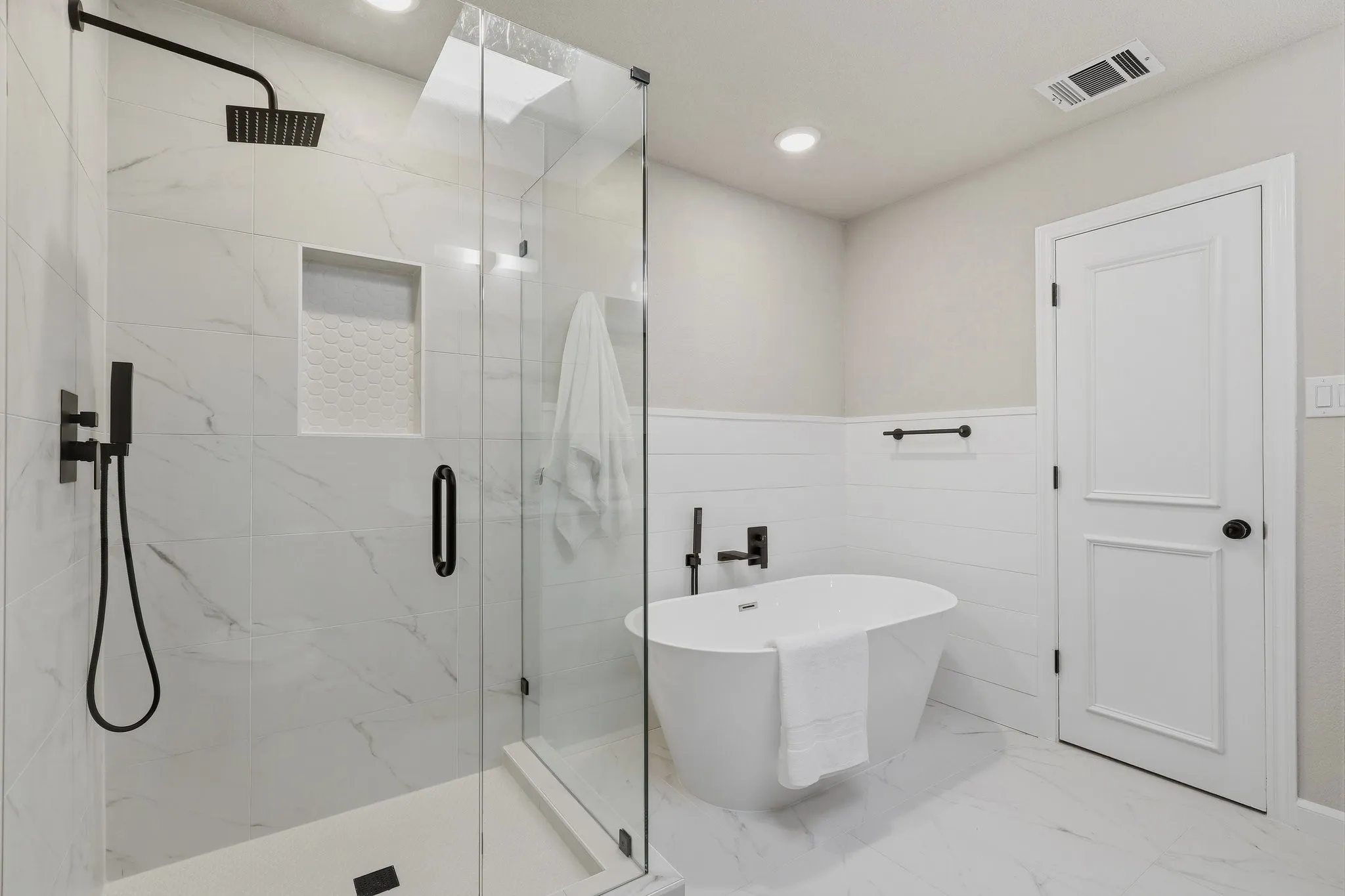 Shower enclosure with clear glass, matte black fixtures, built-in tile niche, and a freestanding soaking tub