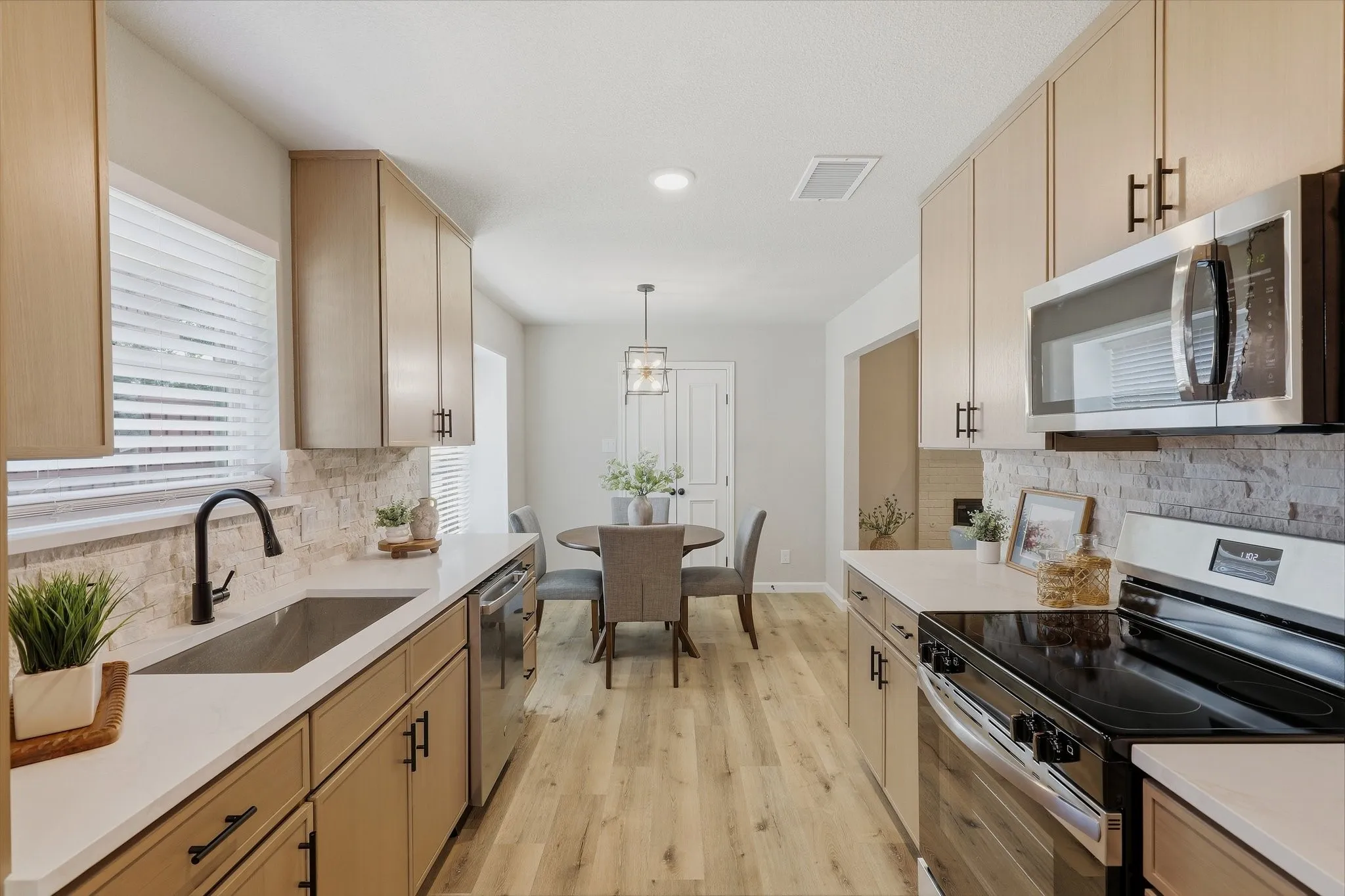 Contemporary kitchen with light wood-finish cabinetry, white countertops, stone-look backsplash, and stainless-steel appliances