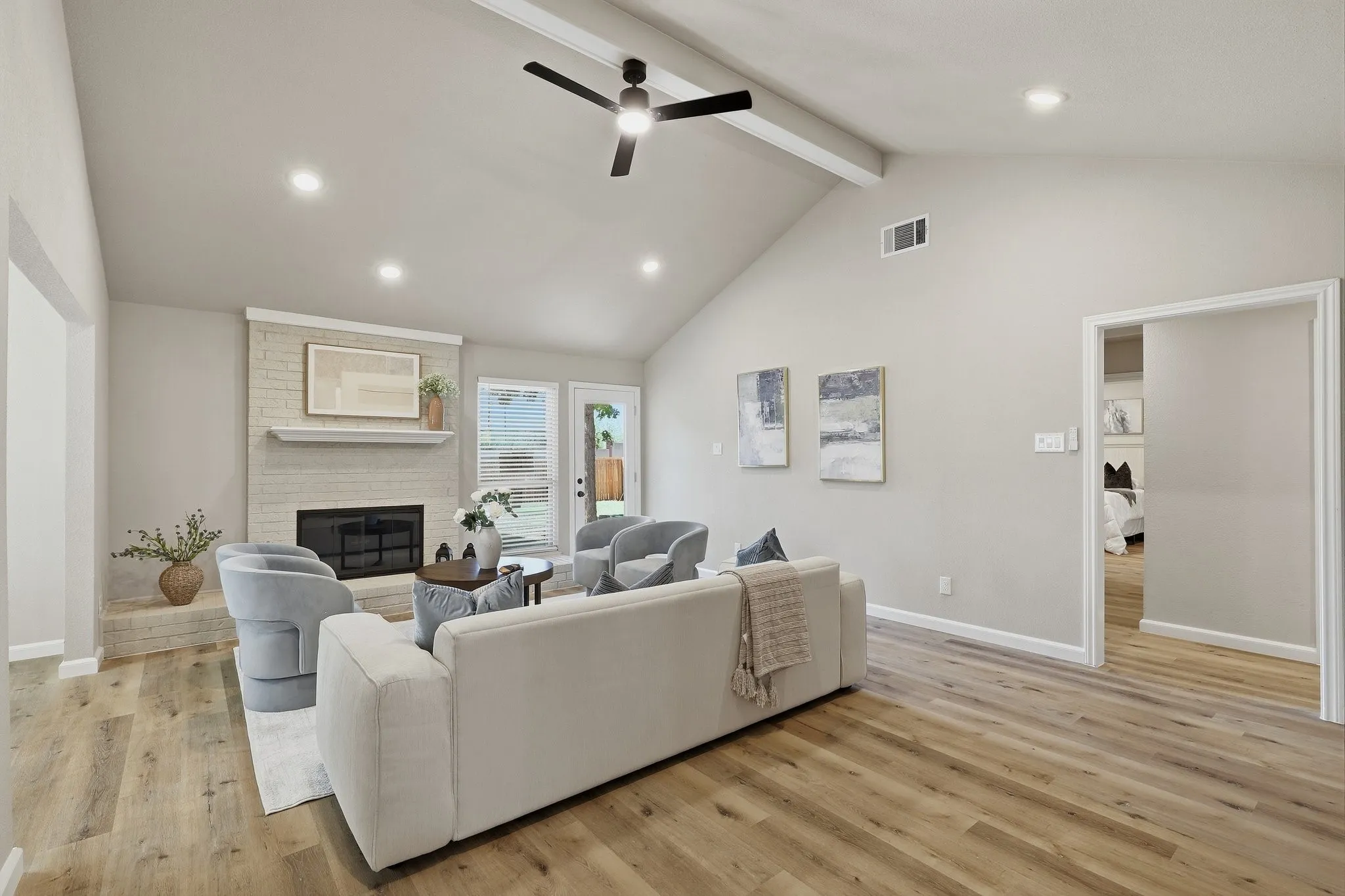 Vaulted ceiling with exposed beams, recessed lighting, wood-finish flooring, brick fireplace, and direct backyard access