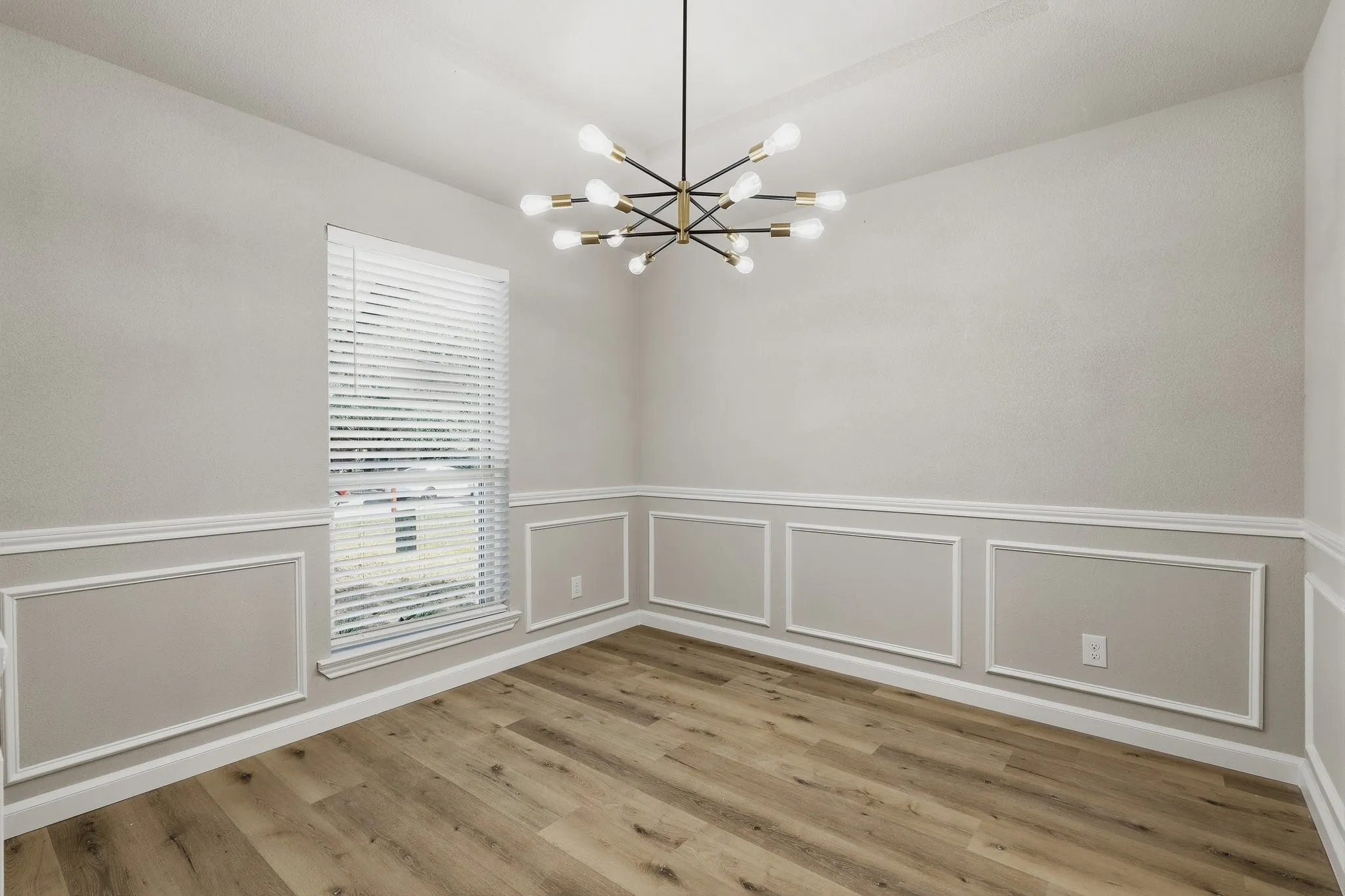 Wood-finish flooring, accent wall paneling, modern sputnik chandelier, and a large window with blinds