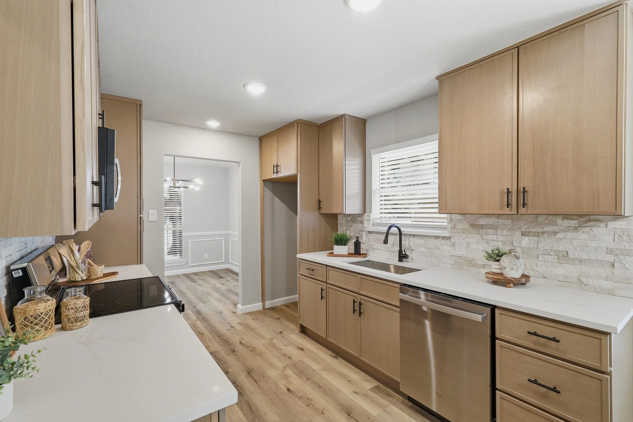 Contemporary kitchen featuring light wood-finish cabinetry, white countertops, stainless steel appliances, a stacked stone backsplash, and wood-finish flooring