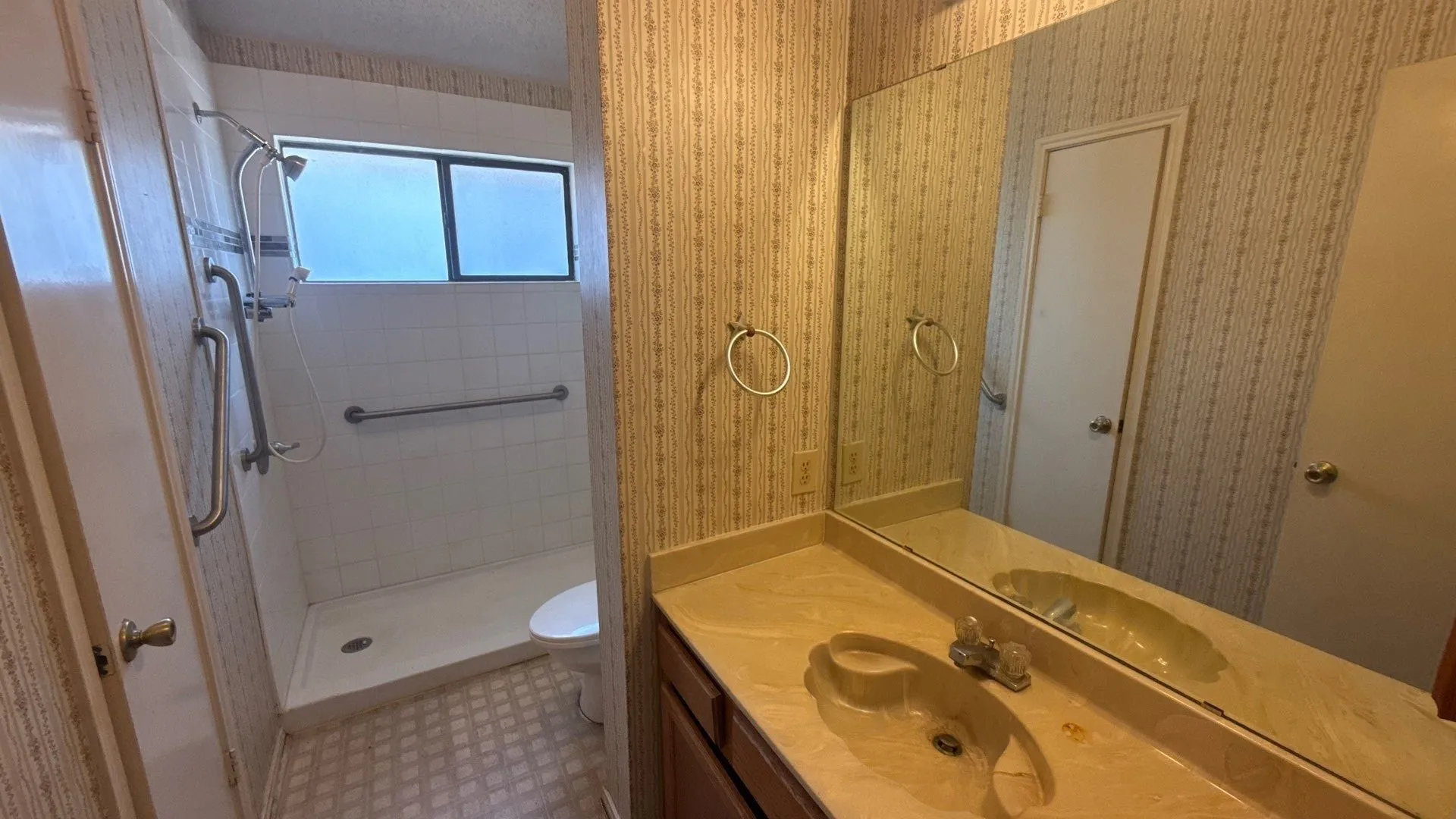 Vanity with integrated sink and chrome faucet, full-width mirror, and a shower with white tile surround and grab bars