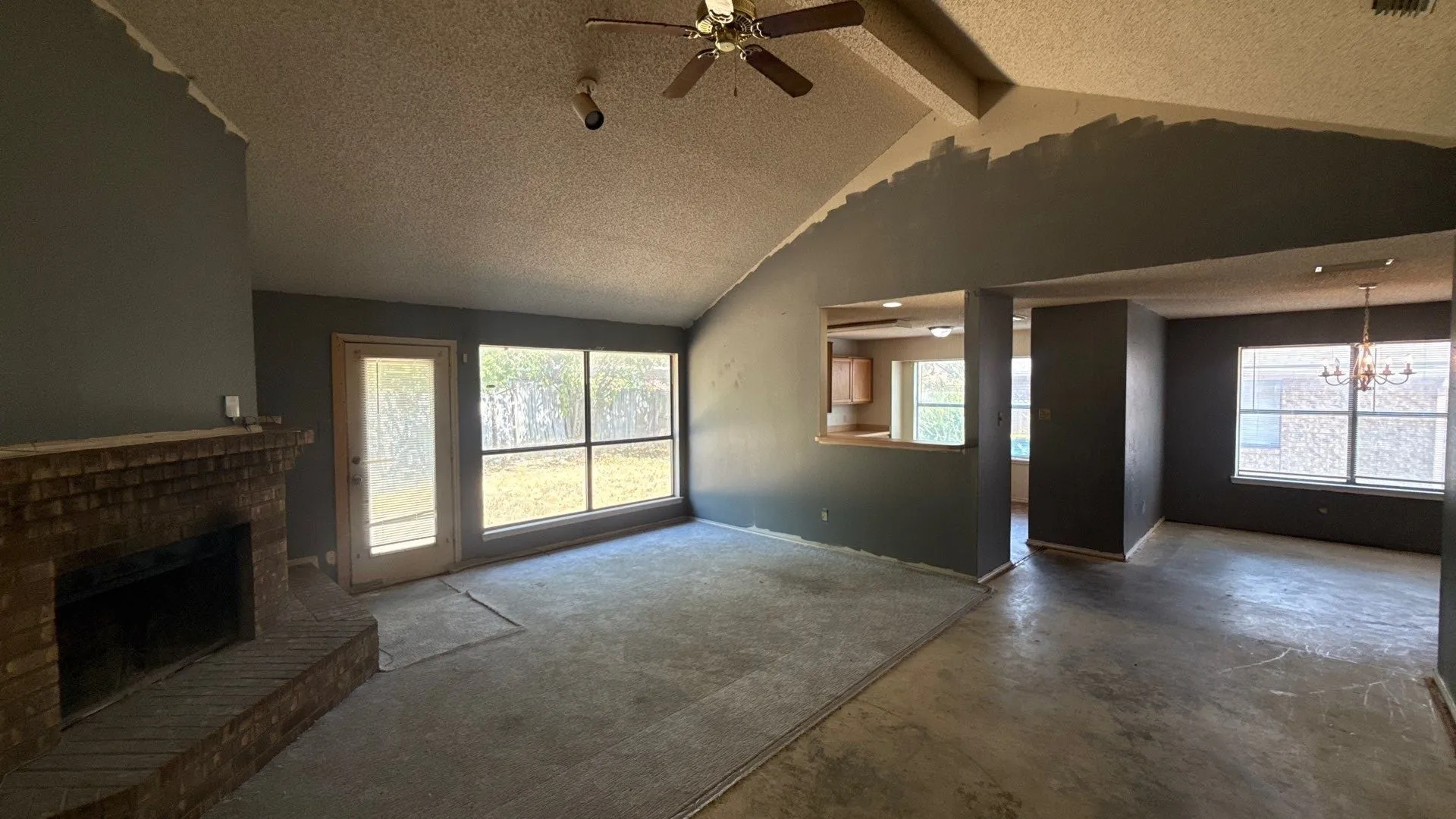 Vaulted ceiling, brick fireplace, expansive window, ceiling fan, and pass-through window