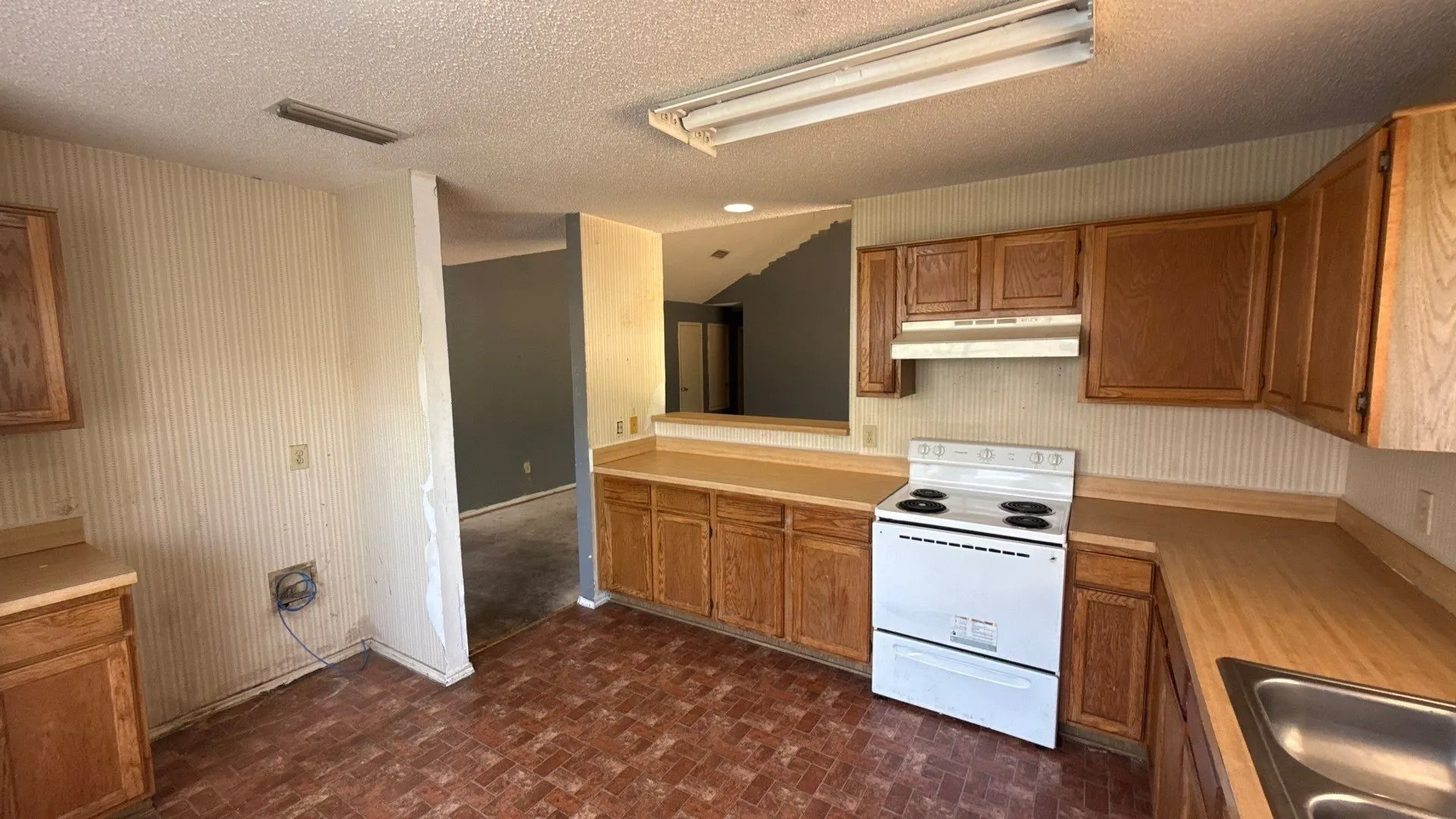 Kitchen with wood-finish cabinetry, built-in stainless steel sink, and white electric range
