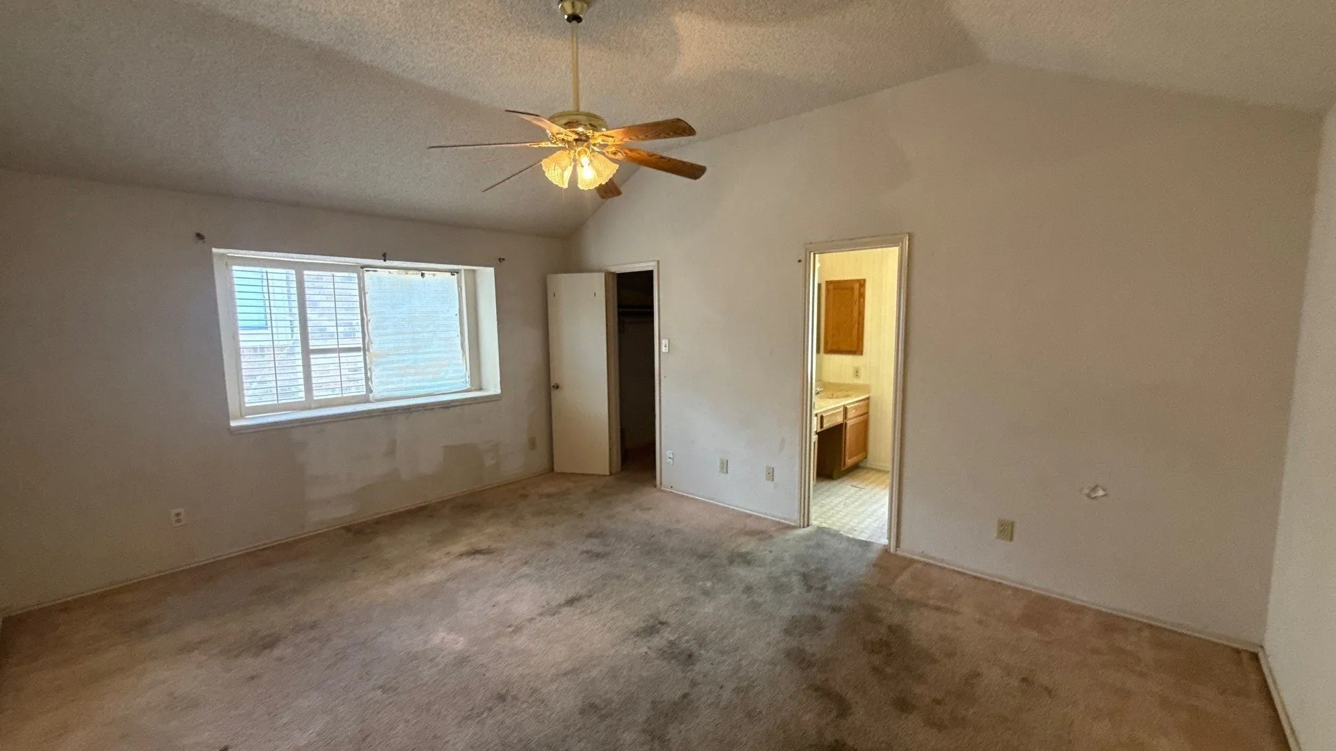 Vaulted ceiling with a ceiling fan, a window with blinds, and an open doorway leading to a bathroom with a vanity and mirror