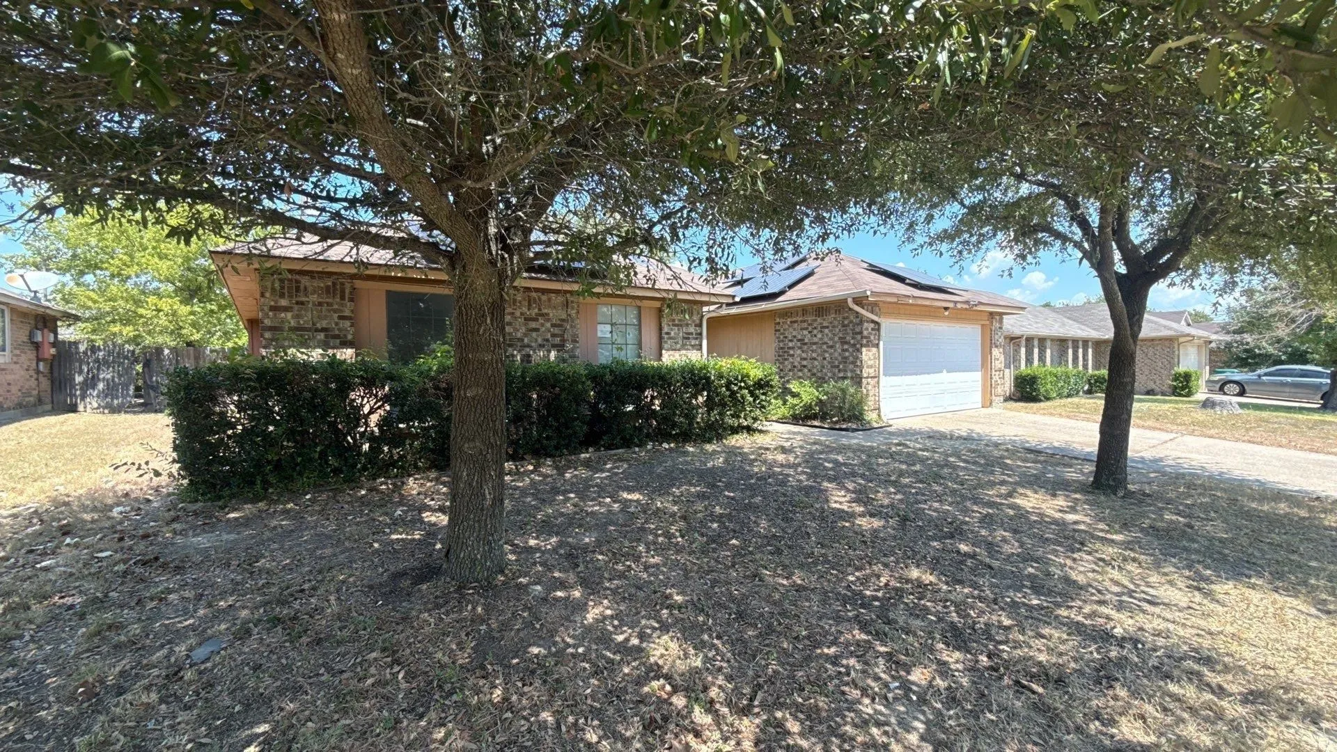 Brick exterior, attached garage, solar panels, mature trees, and a concrete driveway