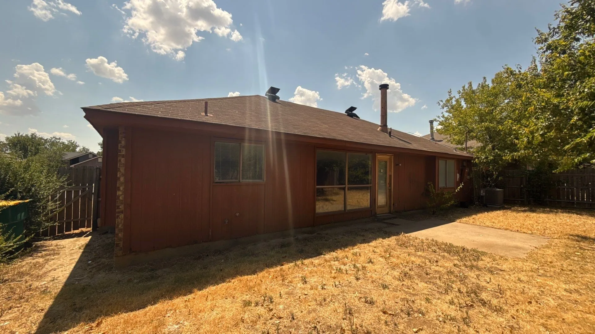 Rear exterior with a concrete patio, wood fence, and mature trees