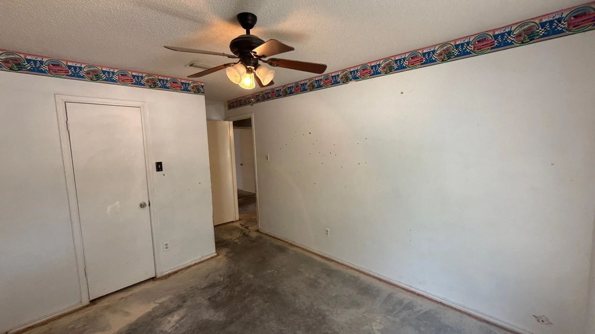 Room featuring a ceiling fan with light fixture, white walls, and a door with a spherical handle