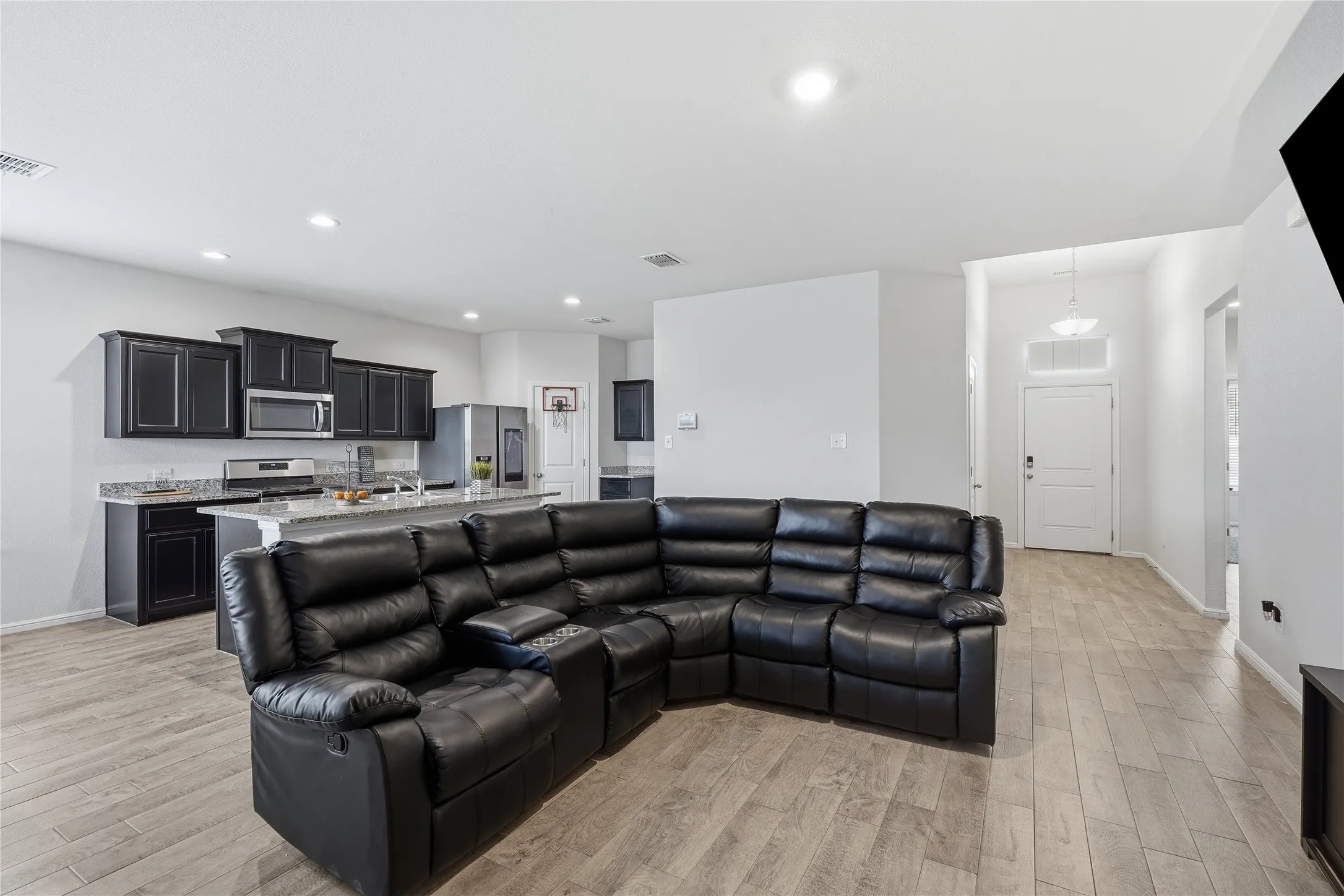 Open-concept interior featuring wood-finish flooring, recessed lighting, shaker-style cabinetry, and a stone-surface island