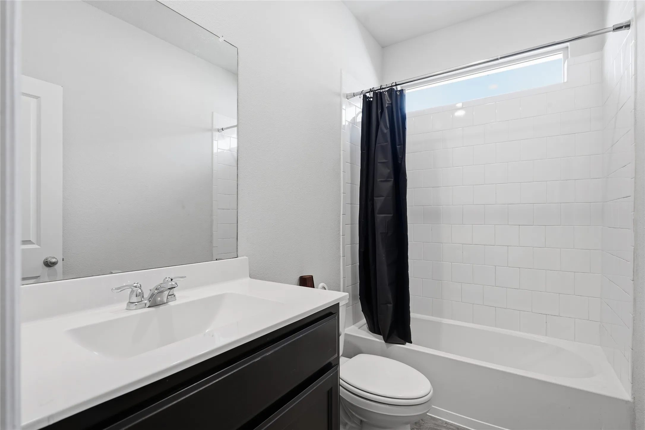 Bathroom featuring a vanity with white countertop and integrated sink, large wall-mounted mirror, tub-shower combination with white subway-style wall tile, and transom window