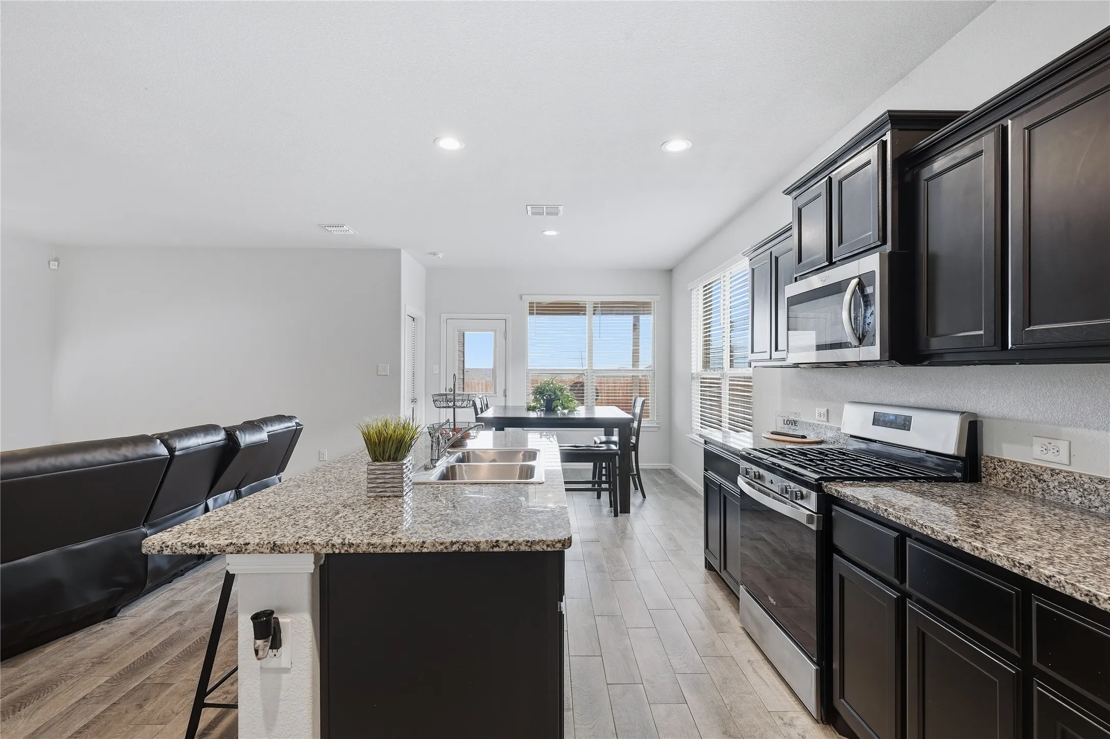 Kitchen featuring dark cabinetry, stone-finish countertops, stainless steel appliances, a center island with a dual-basin sink, and wood-finish flooring