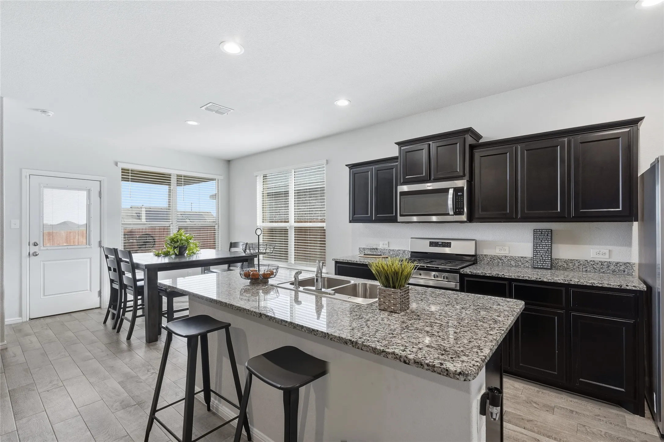 Kitchen featuring dark-finish cabinetry, stone-surface countertops, a center island with an integrated stainless steel dual-basin sink, recessed lighting, and tile flooring