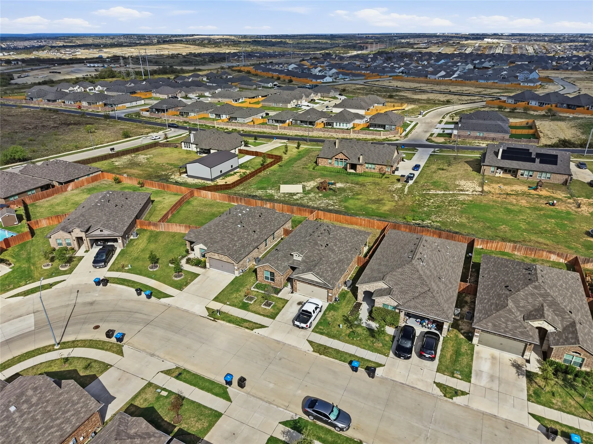 Aerial perspective of a suburban neighborhood featuring paved streets, concrete driveways, detached single-story residences with shingle roofs, and fenced backyards