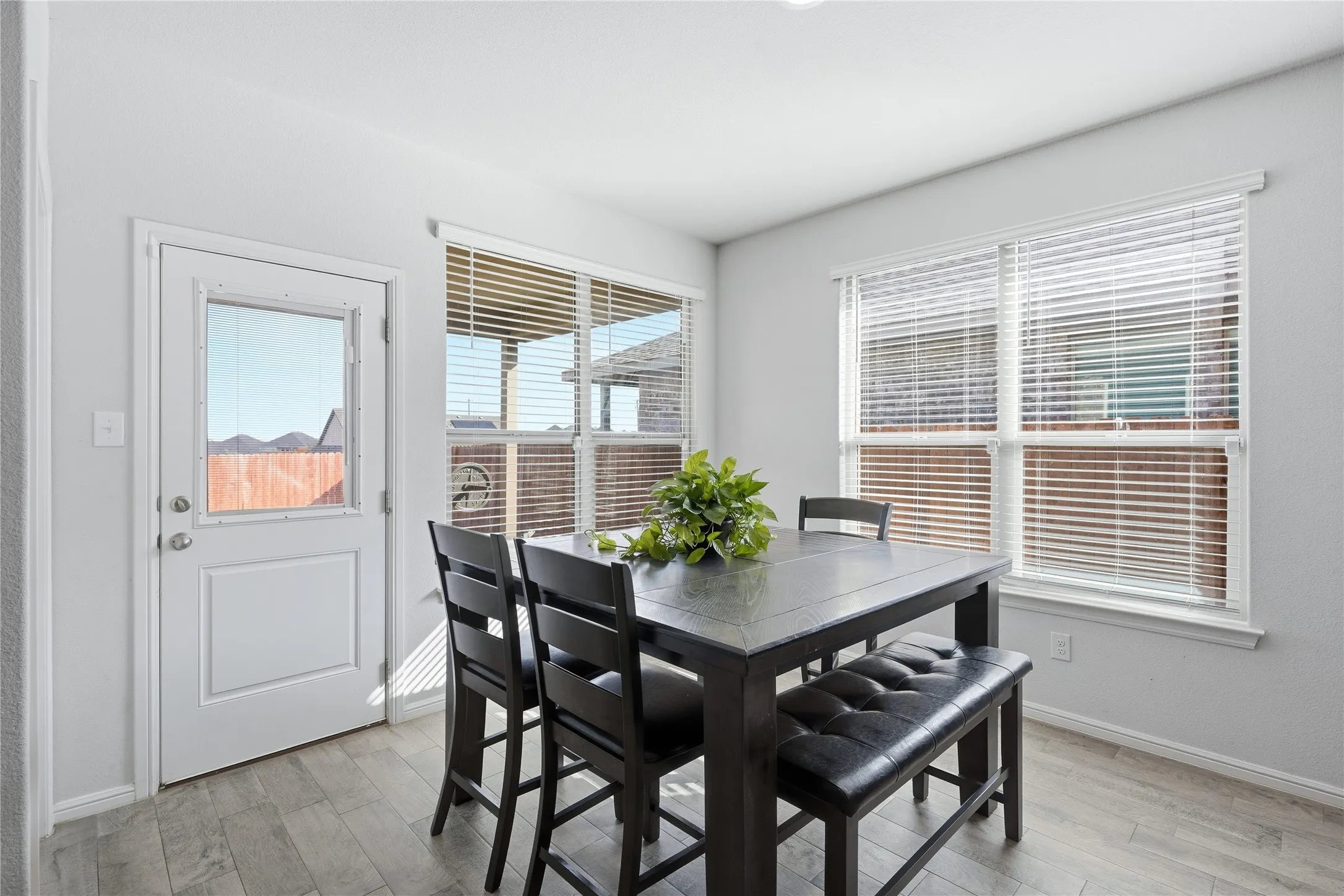 Neutral-toned interior featuring wood-finish tile flooring, multiple dual-pane windows with horizontal blinds, and a rear-entry door with integrated glass paneling
