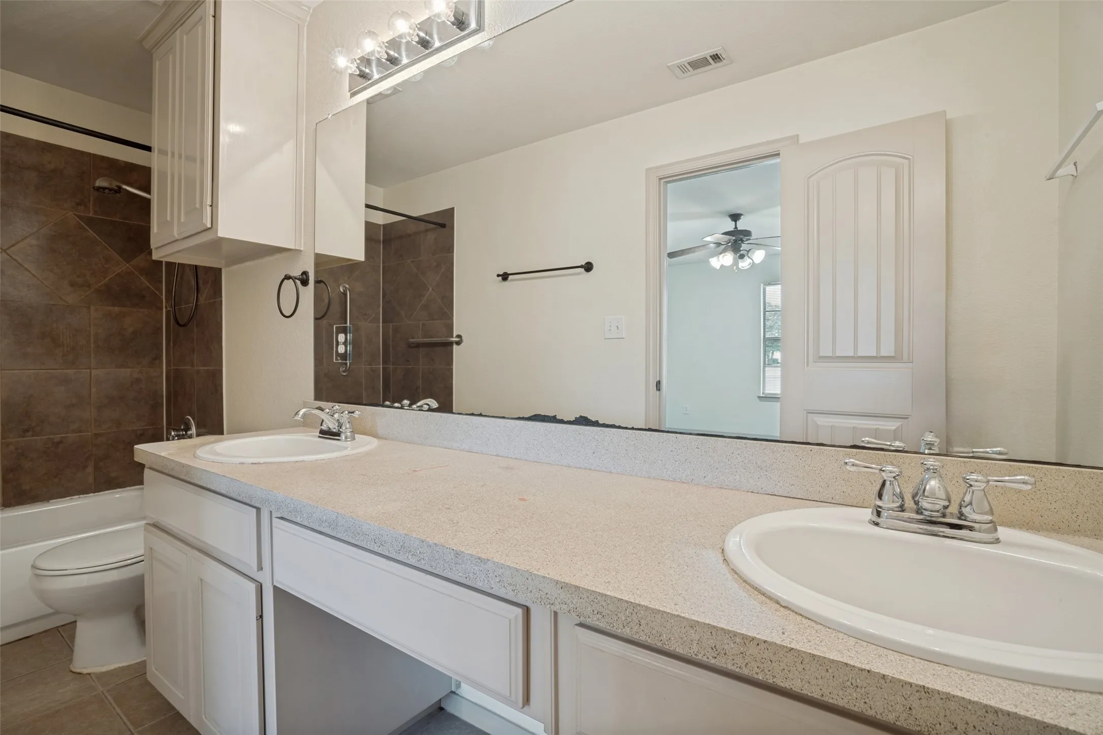 Spacious dual-vanity bathroom featuring an extended countertop with neutral stone surface, recessed lighting, large framed mirror, and chrome faucetry