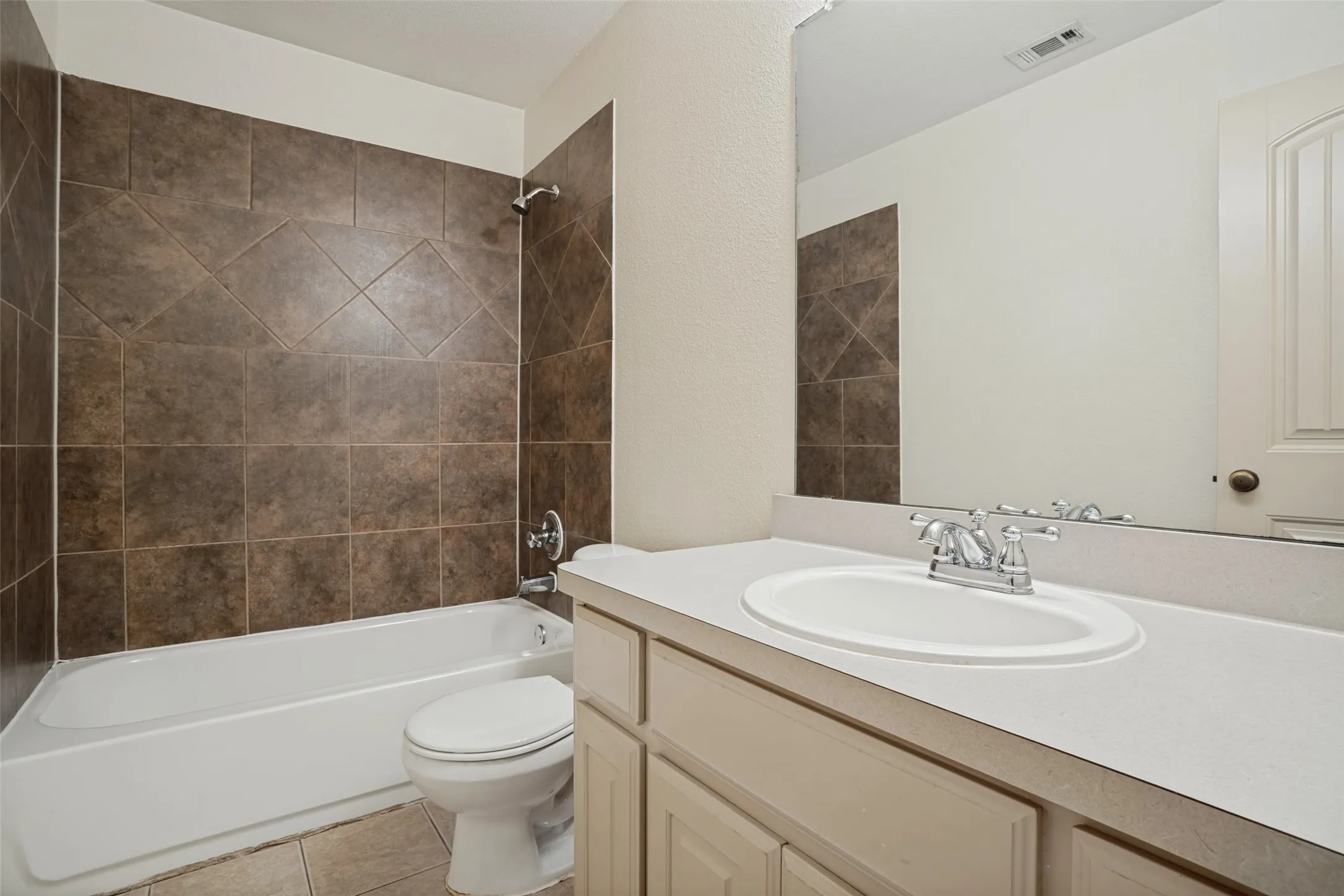 Bathtub with brown tile surround, chrome fixtures, and coordinating floor tile