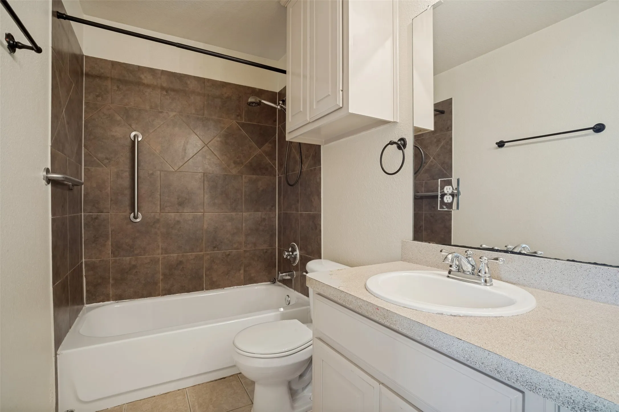 Contemporary bathroom featuring a tile-lined shower enclosure with frameless glass panel and chrome fixtures, white porcelain sink set into a light-finish vanity with ample countertop space, and ceramic tile flooring throughout