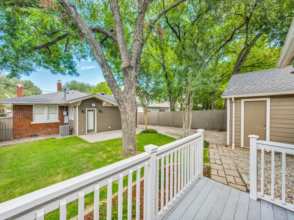 Expansive green lawn, mature trees, brick and siding exterior, exterior storage building, and a paved walkway