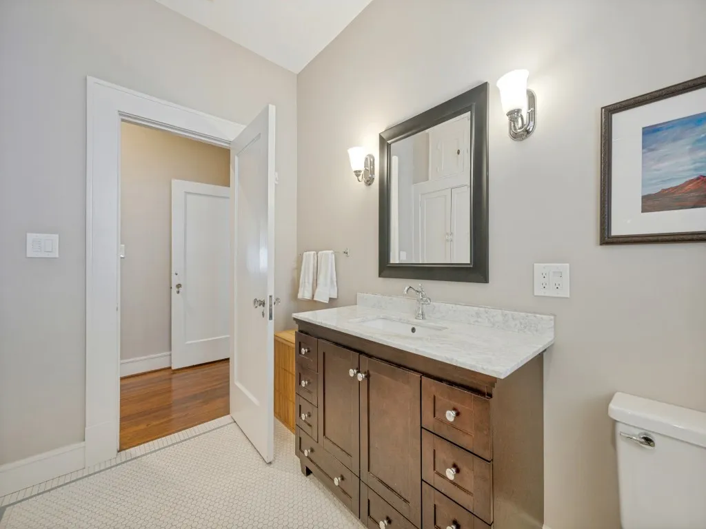 Dark wood-finish vanity with a white countertop and integrated sink, complemented by a framed mirror and wall-mounted sconces