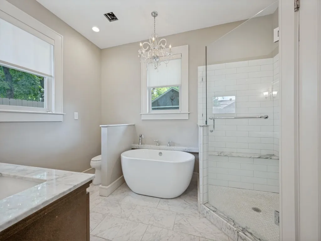 Freestanding bathtub, glass-enclosed shower with subway tile, built-in shower bench, recessed lighting, and a chandelier