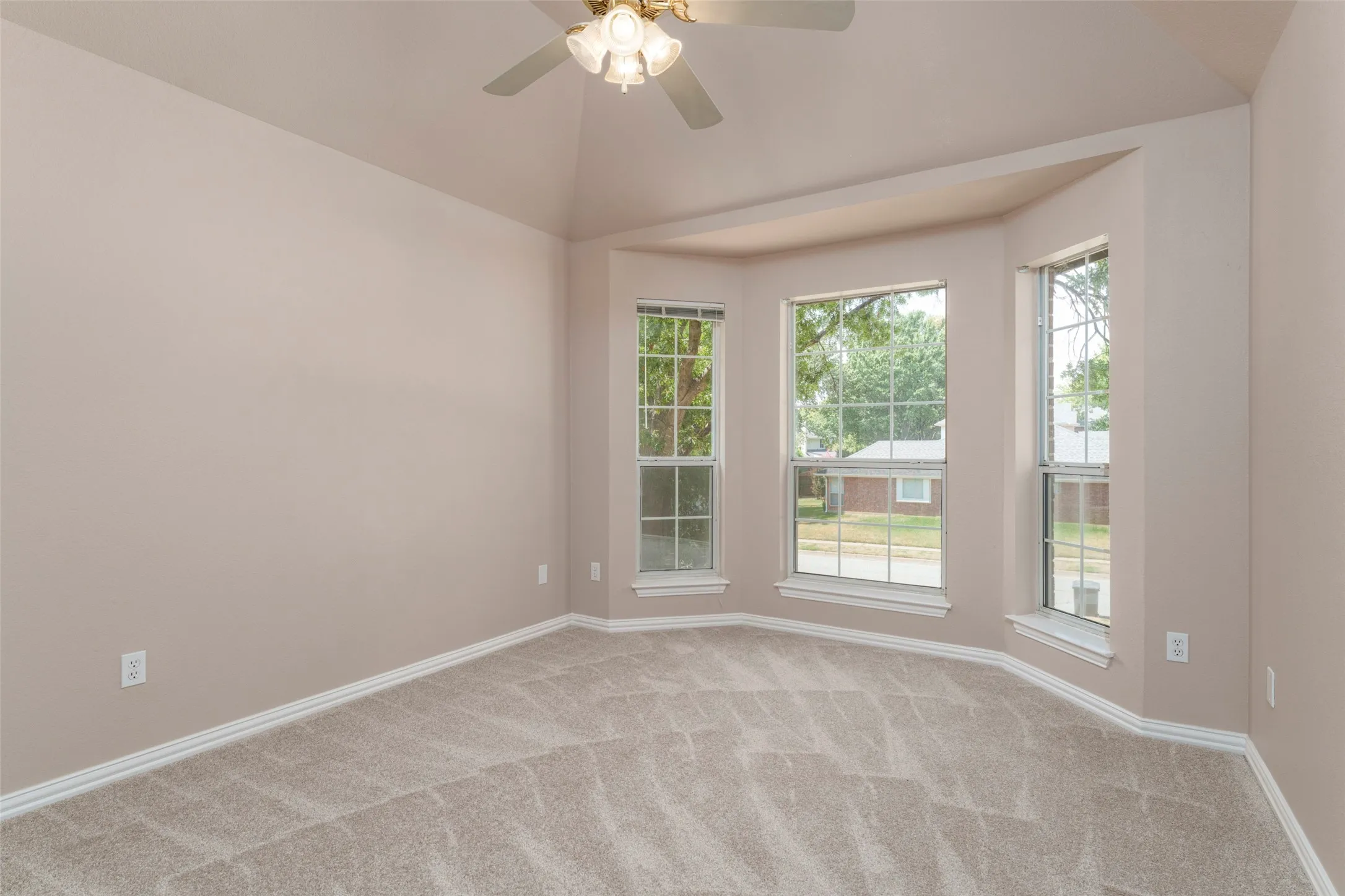 Vaulted ceiling, ceiling fan with integrated lighting, bay window, light-toned carpeting, and neutral wall tones