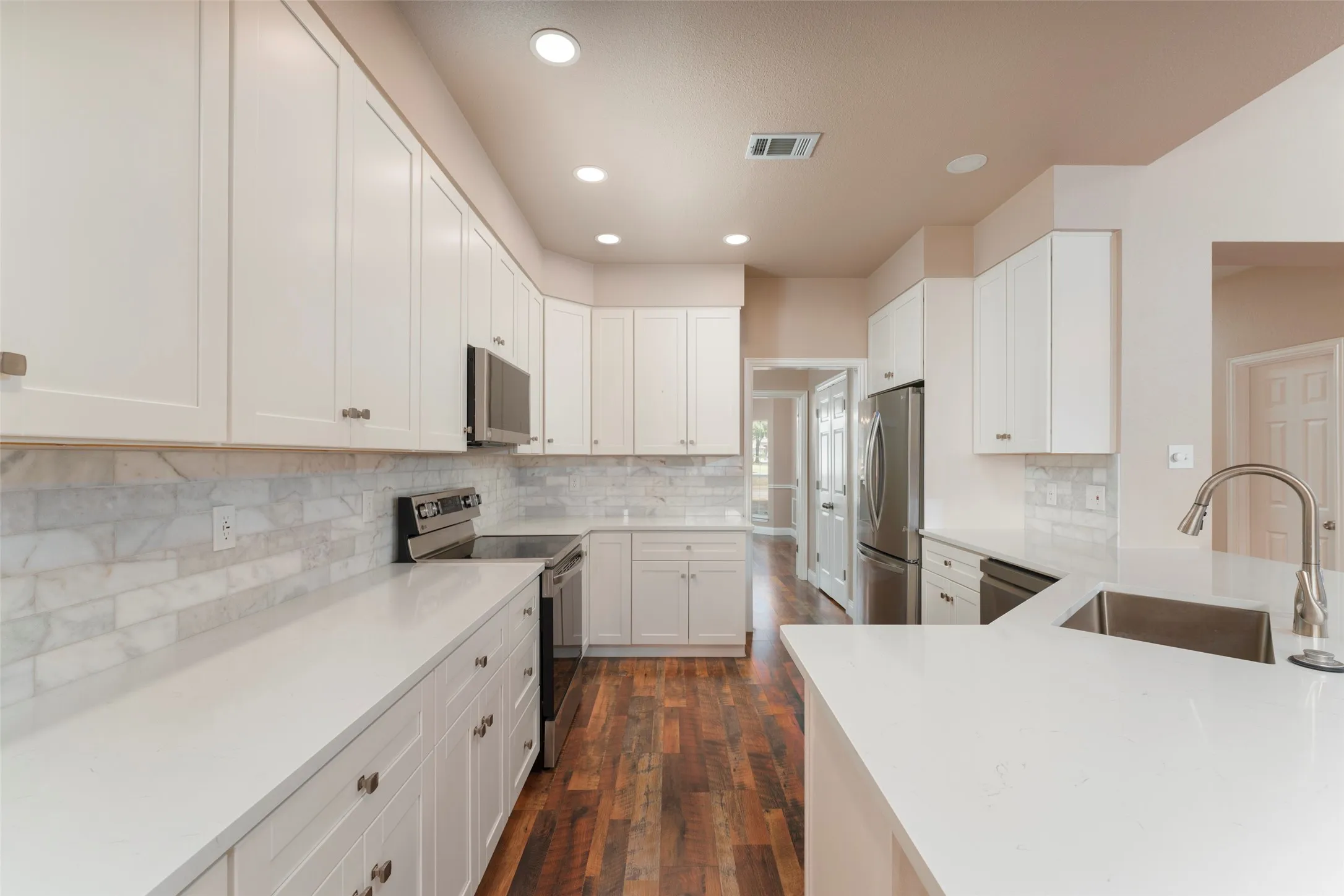 White shaker cabinetry, light-toned countertops, subway tile backsplash, stainless steel appliances, and dark wood-finish flooring