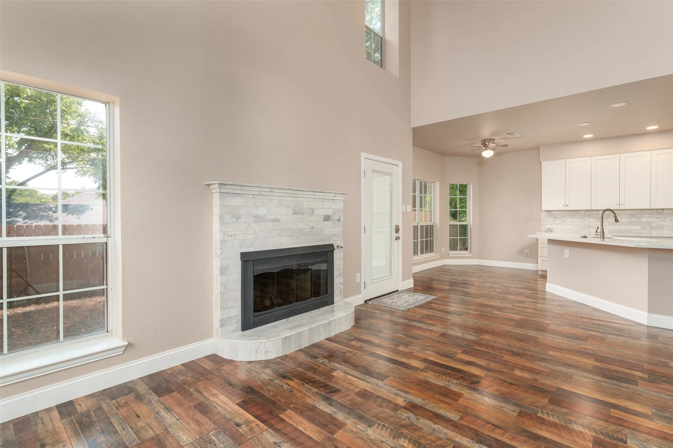 Open-concept living space featuring wood-finish flooring, a contemporary fireplace with a stone surround, and an integrated kitchen with white cabinetry and a breakfast bar