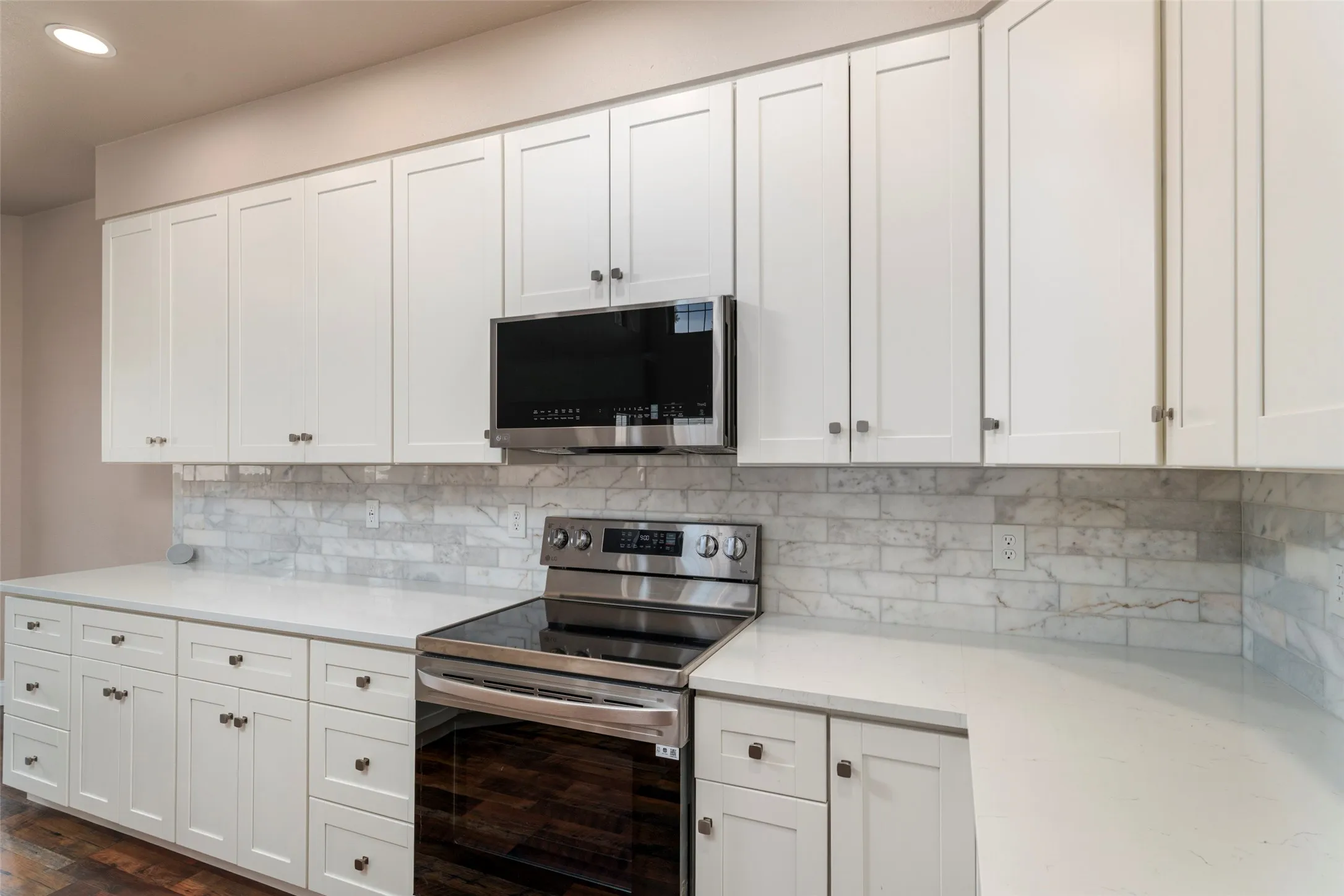 White shaker-style cabinetry, stainless steel range with a built-in microwave, white countertops, and a subway tile backsplash