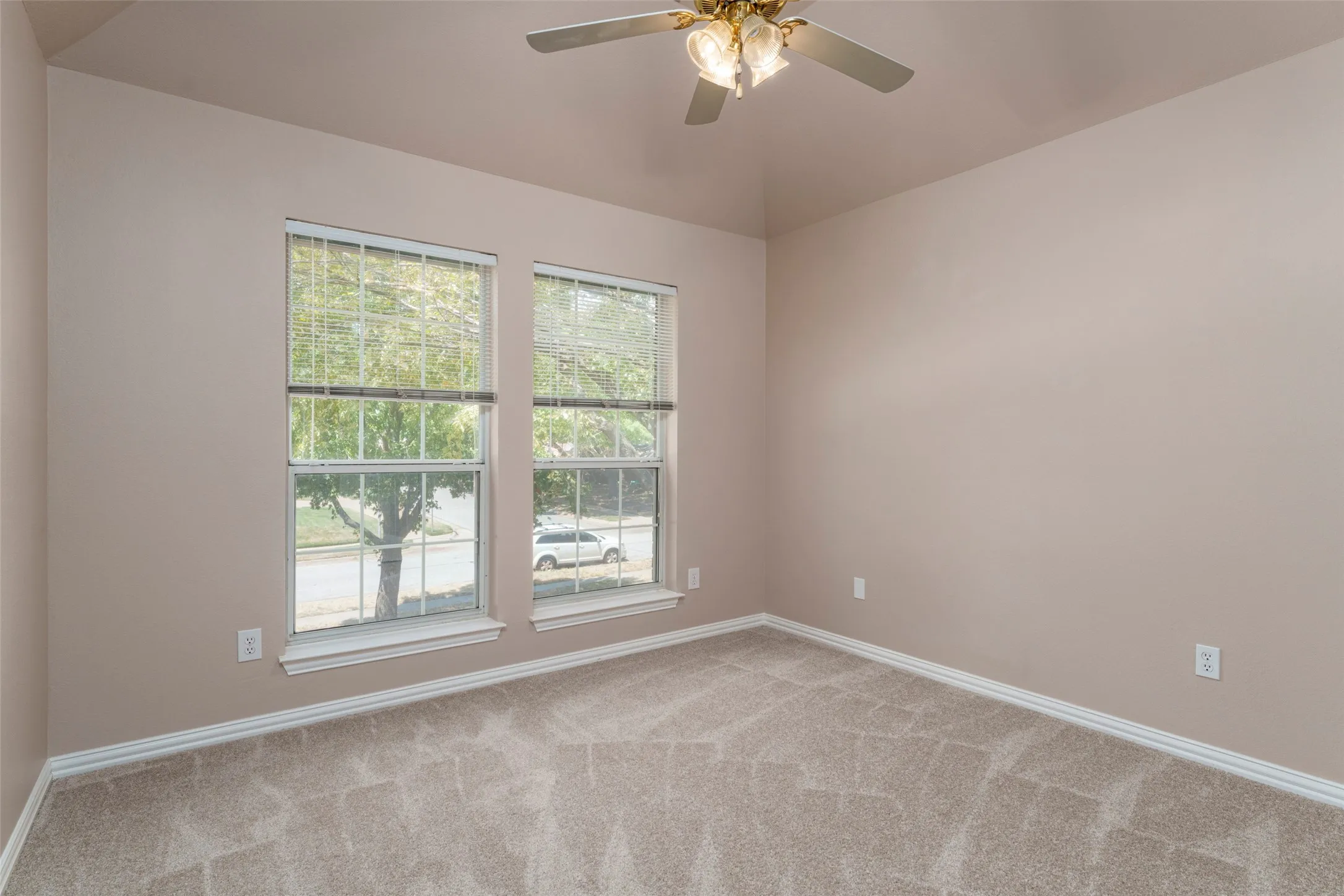 Vaulted ceiling, ceiling fan with integrated lighting, two double-hung windows, neutral-toned wall paint, and light-colored carpet flooring