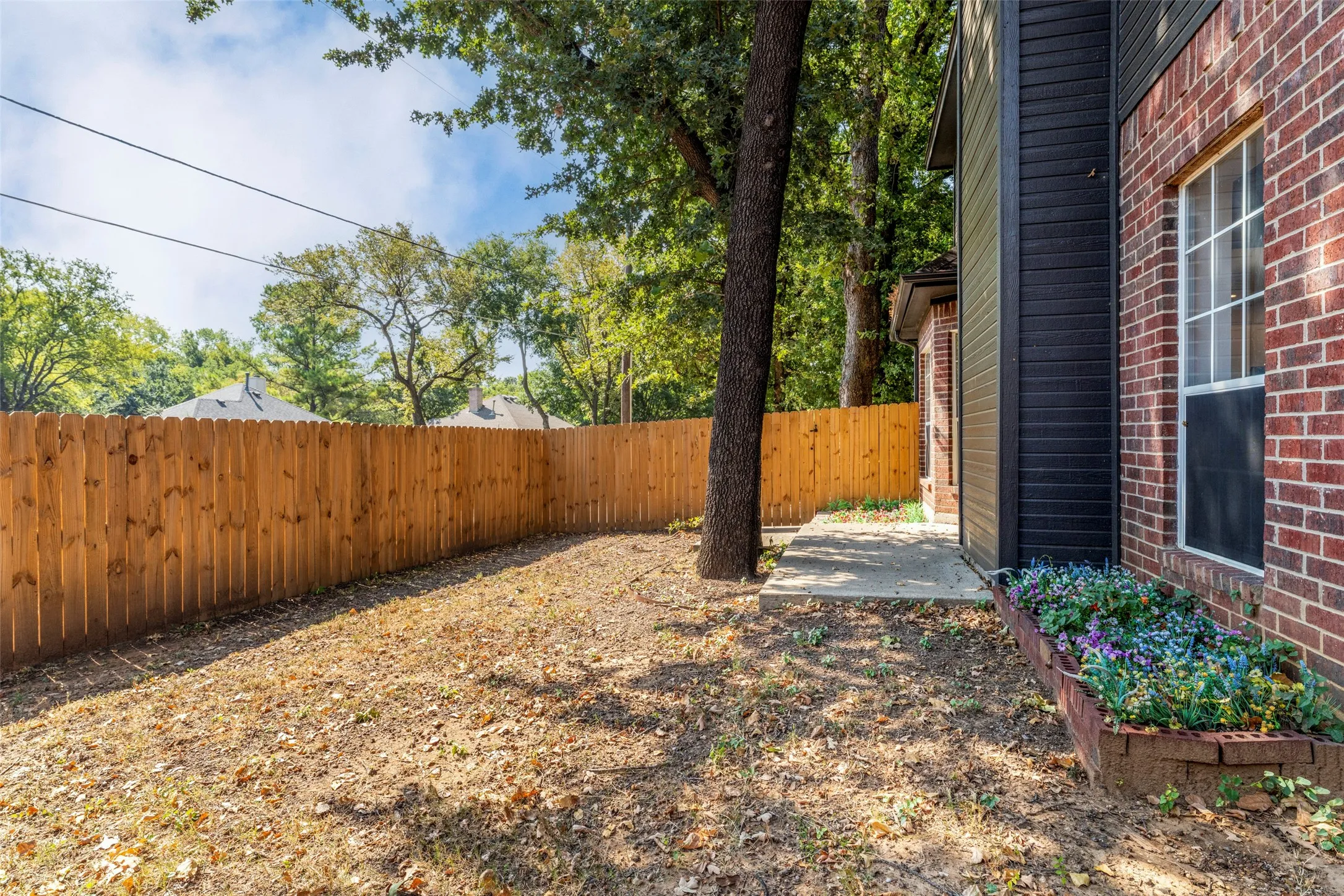 Private backyard with a wood fence, mature trees, and a concrete patio