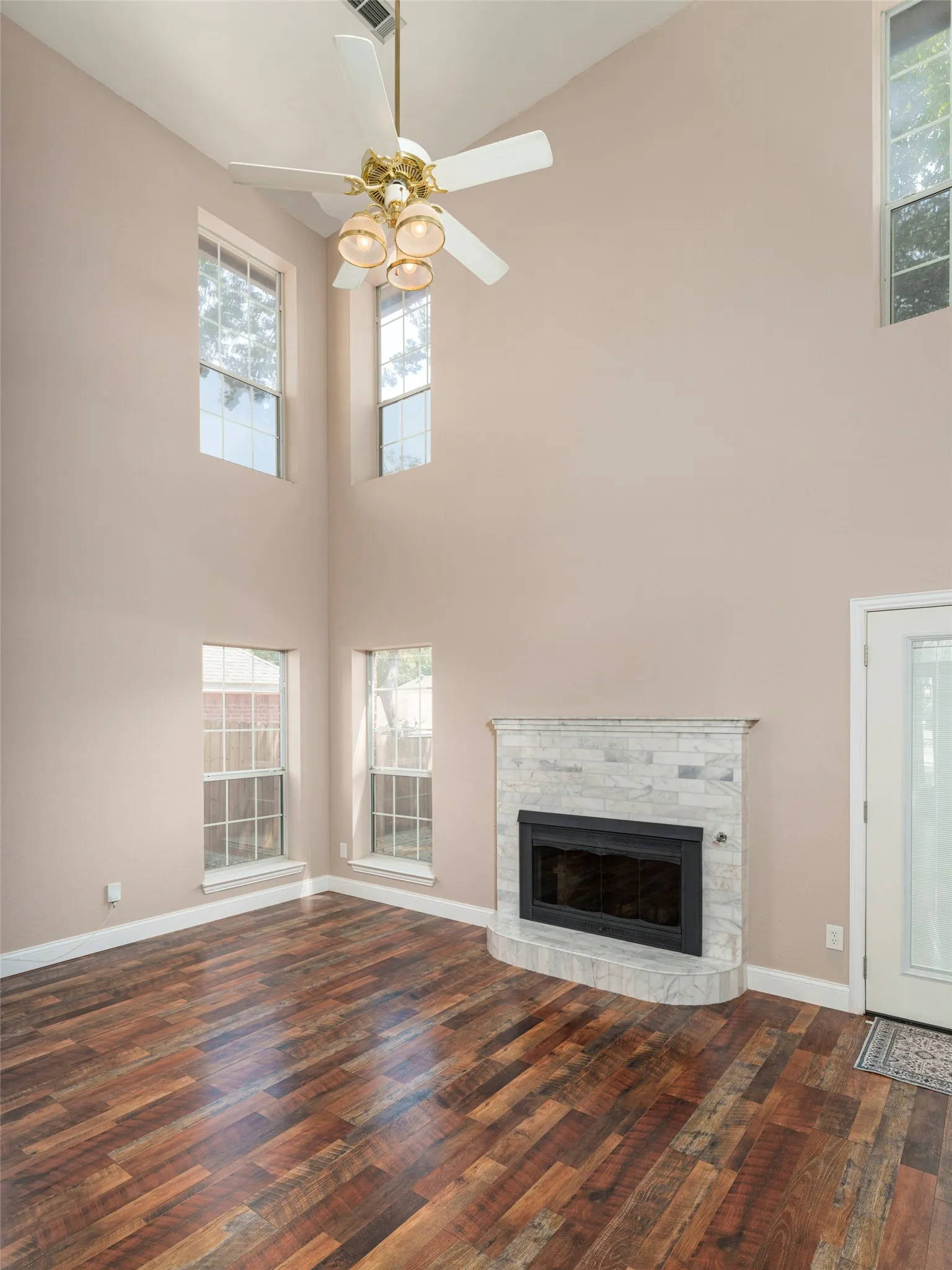 Vaulted ceiling with a ceiling fan light fixture, stone-clad fireplace, and wood-finish flooring