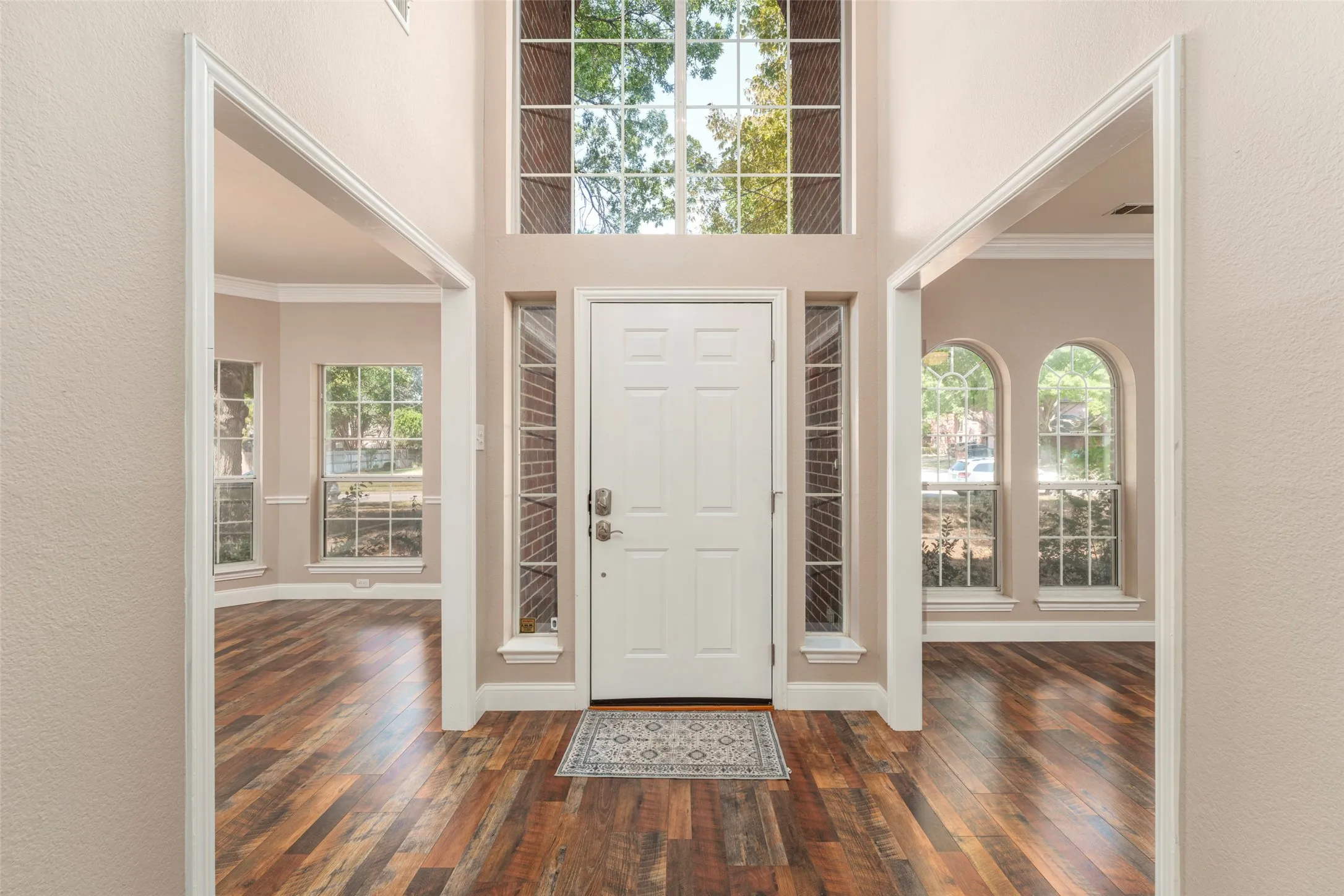 Two-story entry with wood-finish flooring, a white paneled door, and sidelight windows