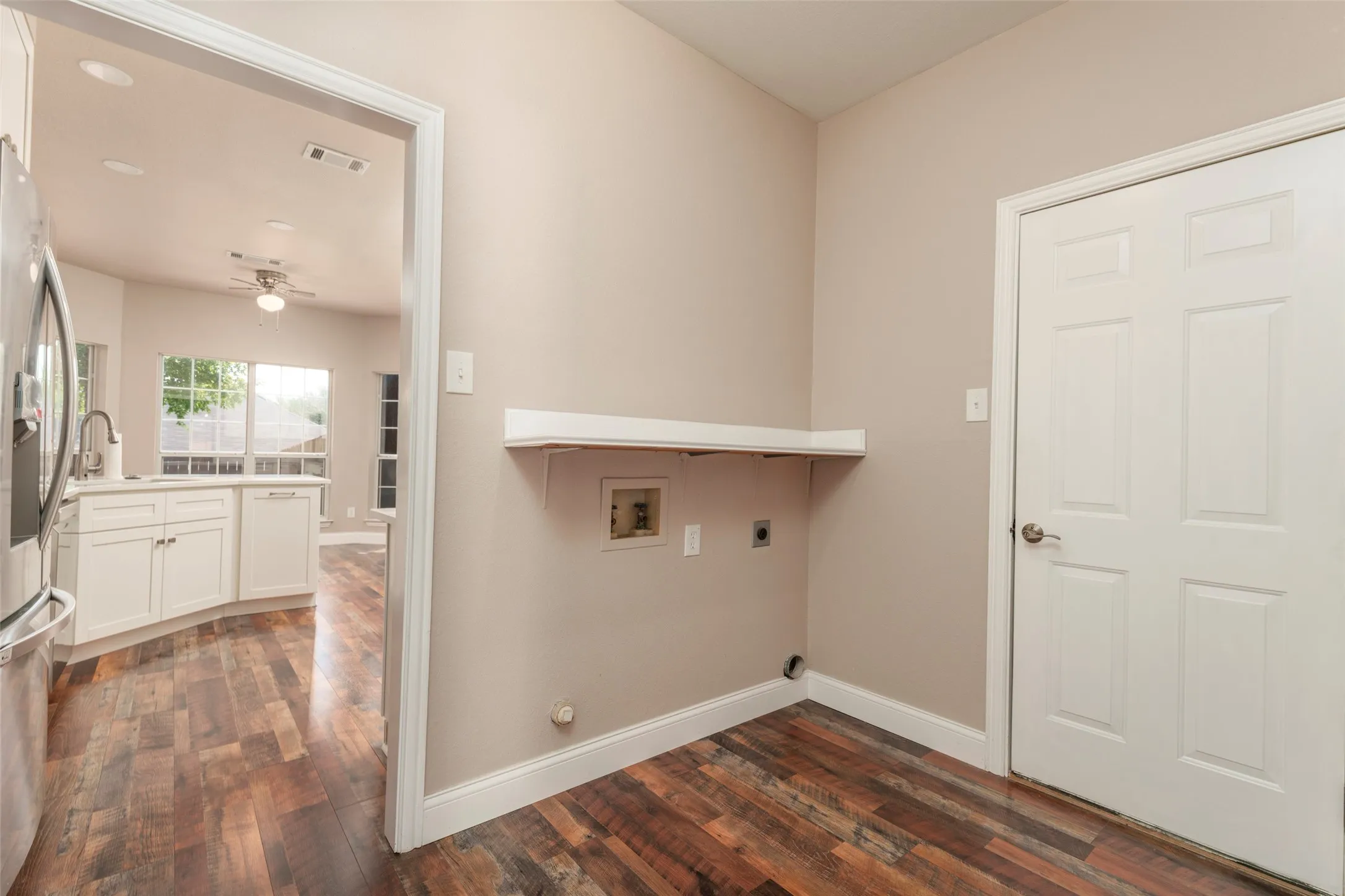 Laundry area with wood-finish flooring, a white shelf, and a white paneled door