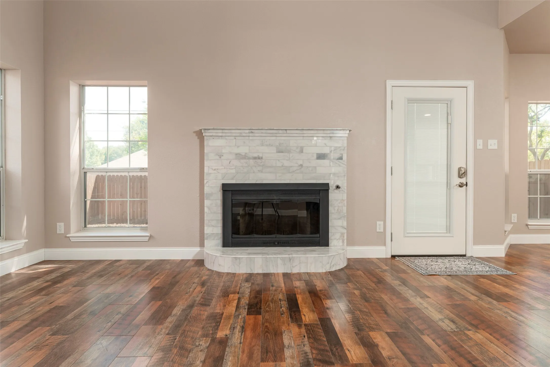 Hardwood flooring throughout, a fireplace with a tiled surround, a glass-paneled exterior door, and multiple windows