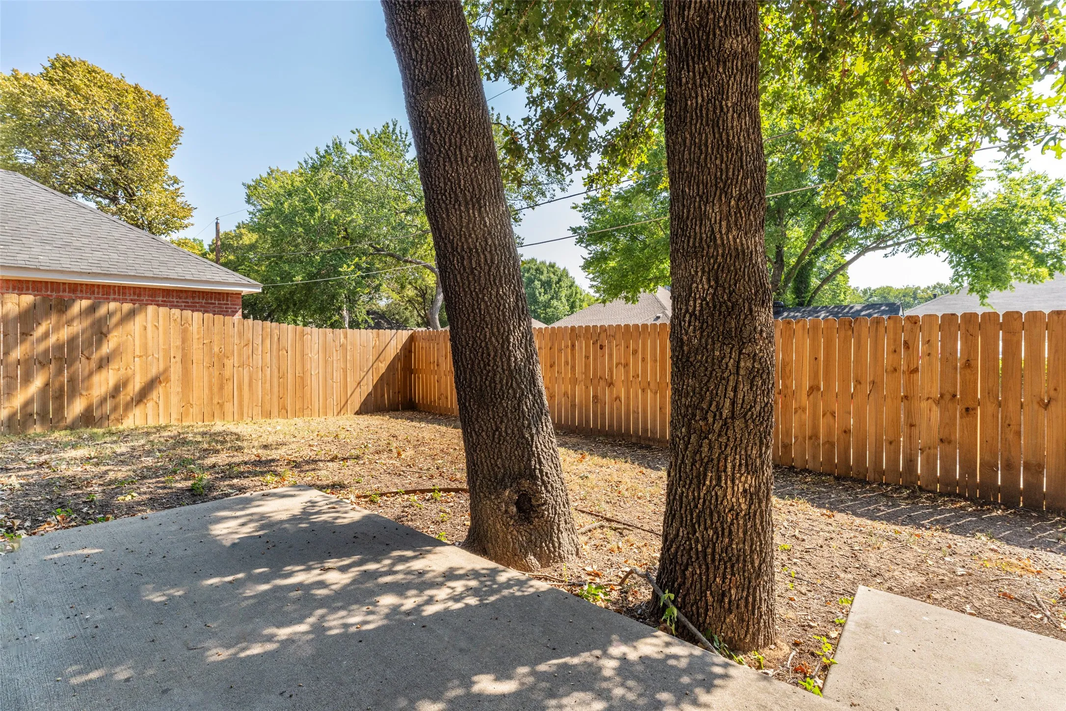 Private backyard space with a new wood fence, mature trees, and a concrete patio