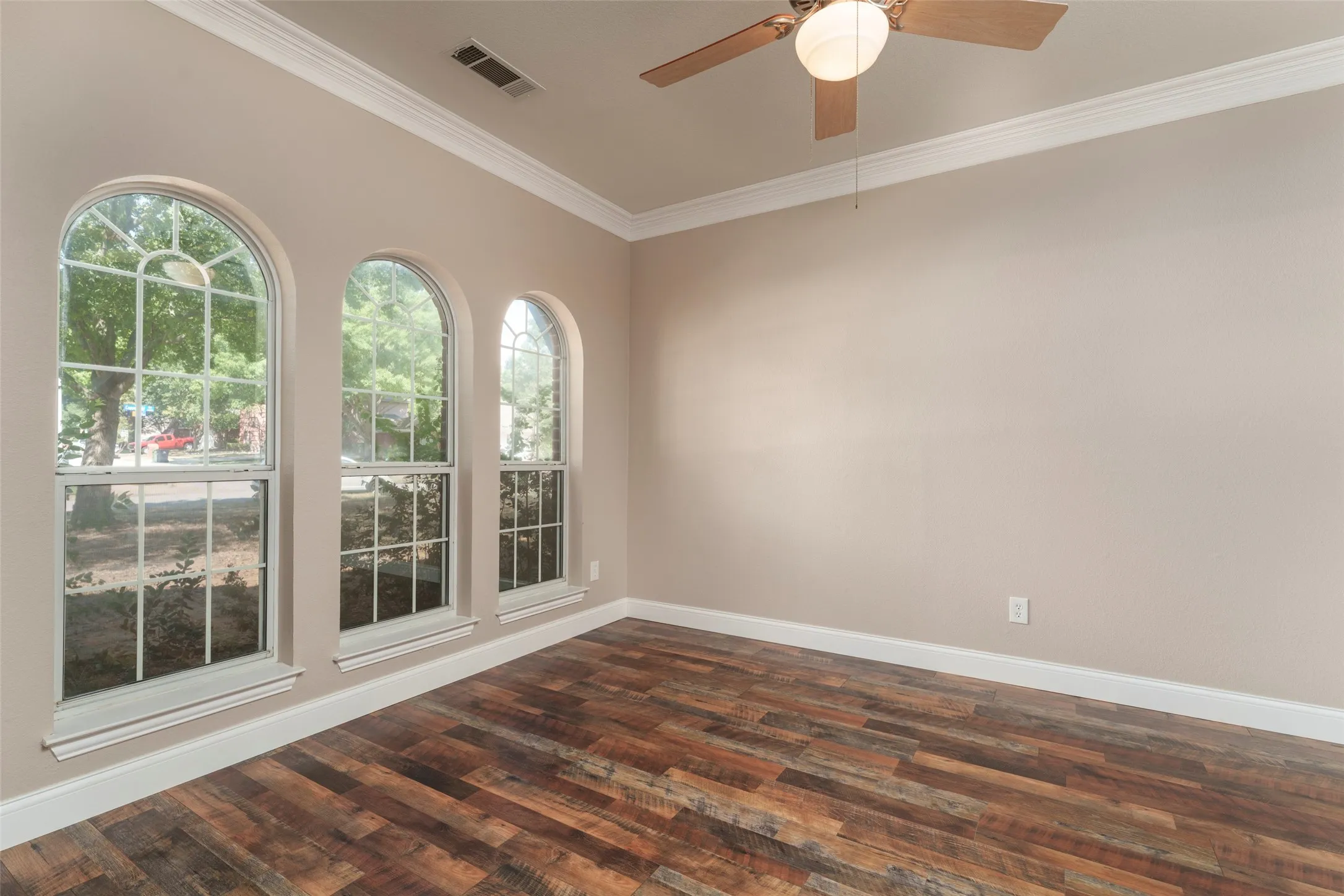 Arched windows with grid patterns, wood-finish flooring, crown molding, and a ceiling fan with integrated lighting