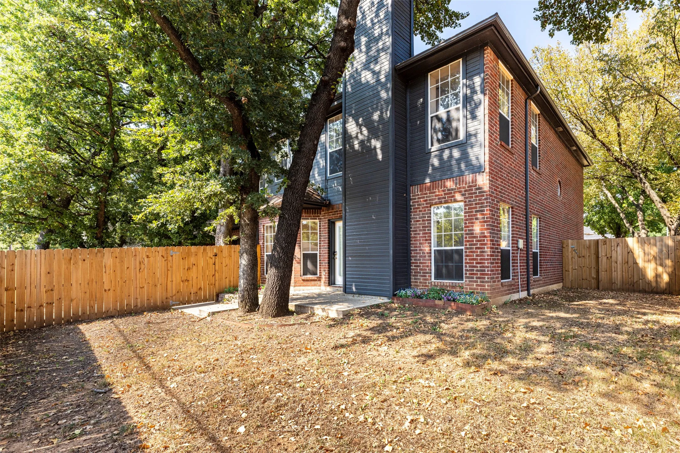Brick exterior with dark siding accents, double-hung windows, and a wood privacy fence