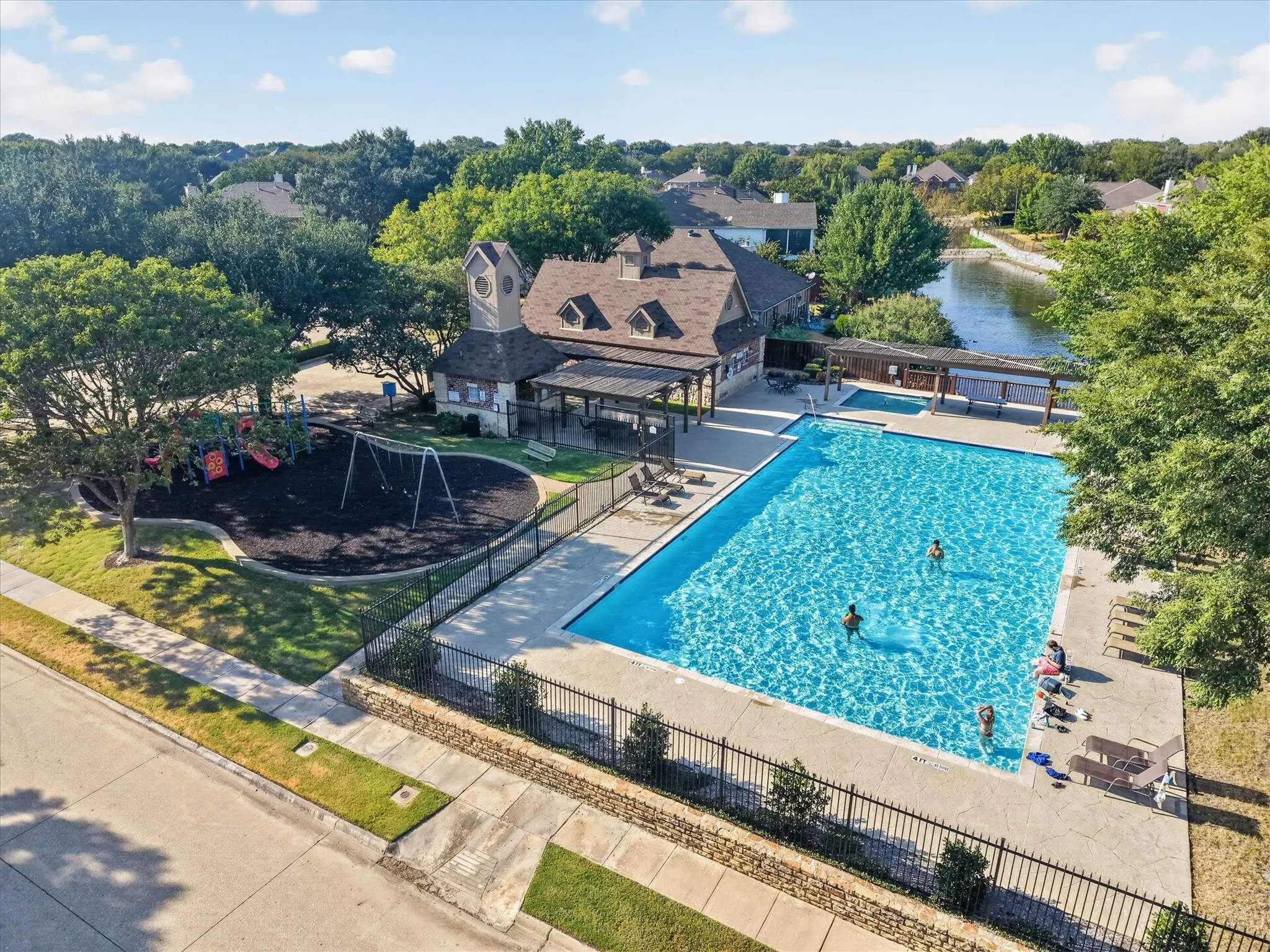 Community swimming pool with an integrated spa, adjacent playground, and a covered patio area, all set against a tranquil water feature
