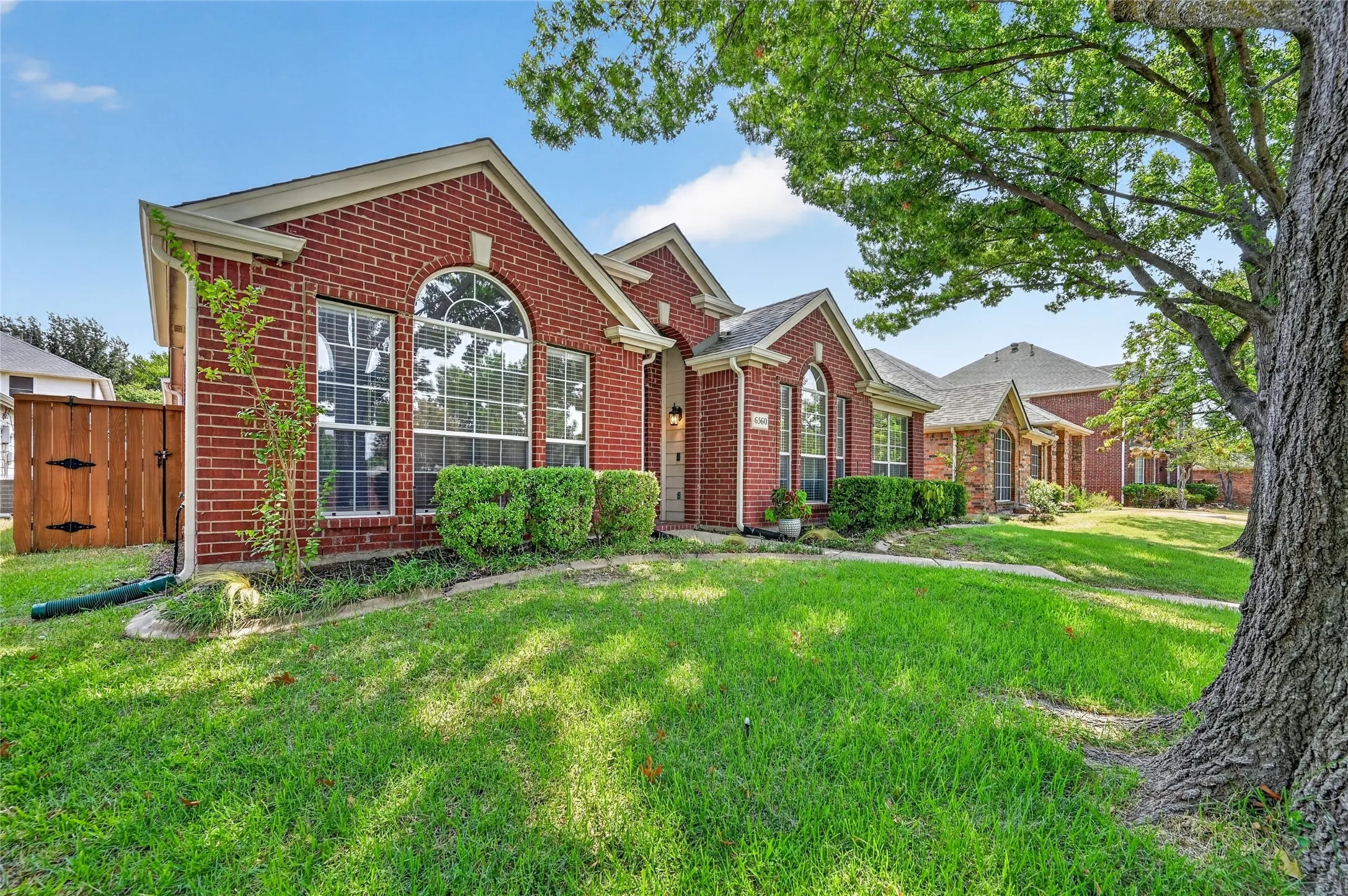 Red brick exterior featuring arched windows, pitched gables, and a mature tree