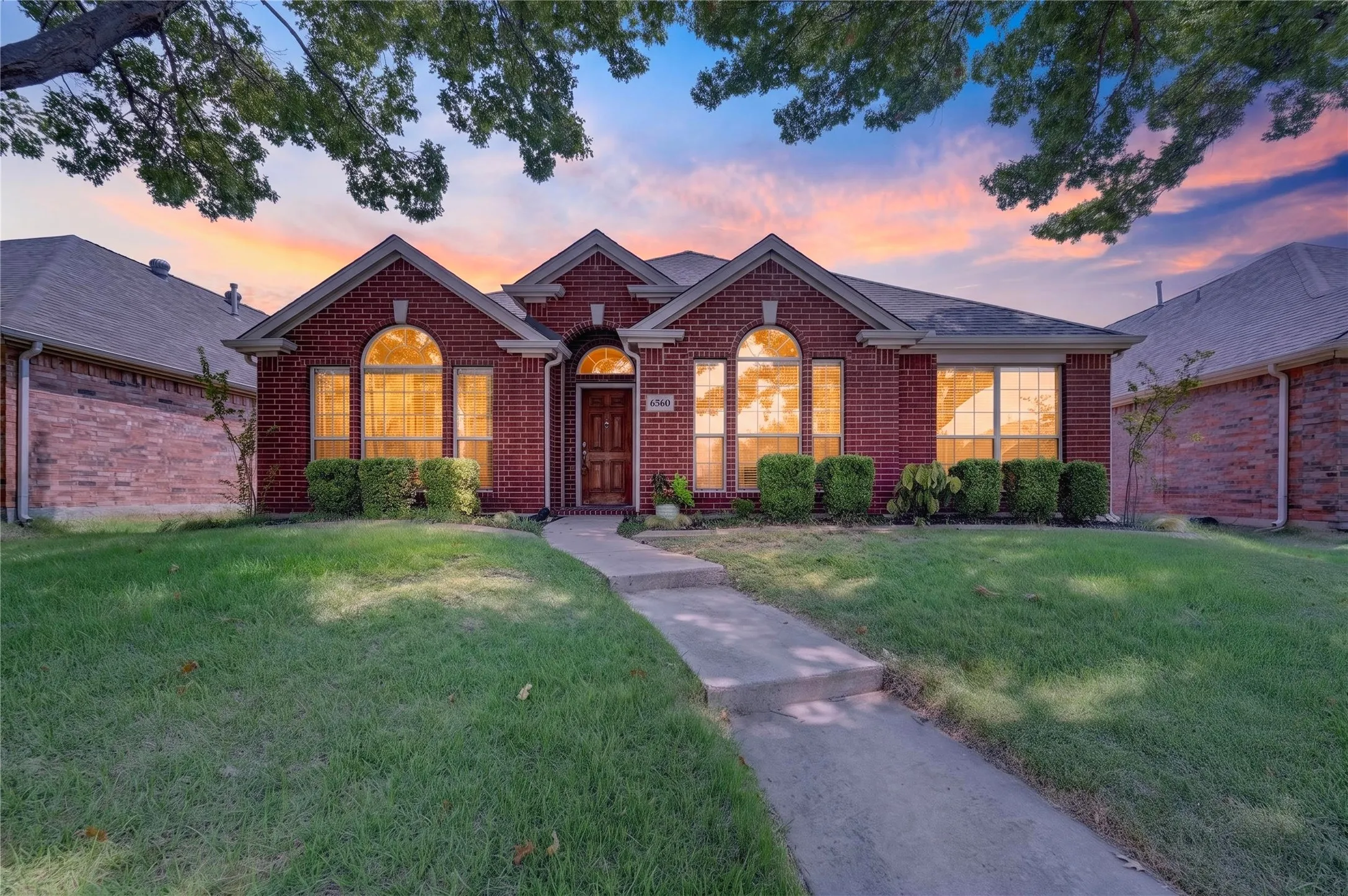 Traditional brick exterior with arched windows, mature landscaping, and an inviting entryway