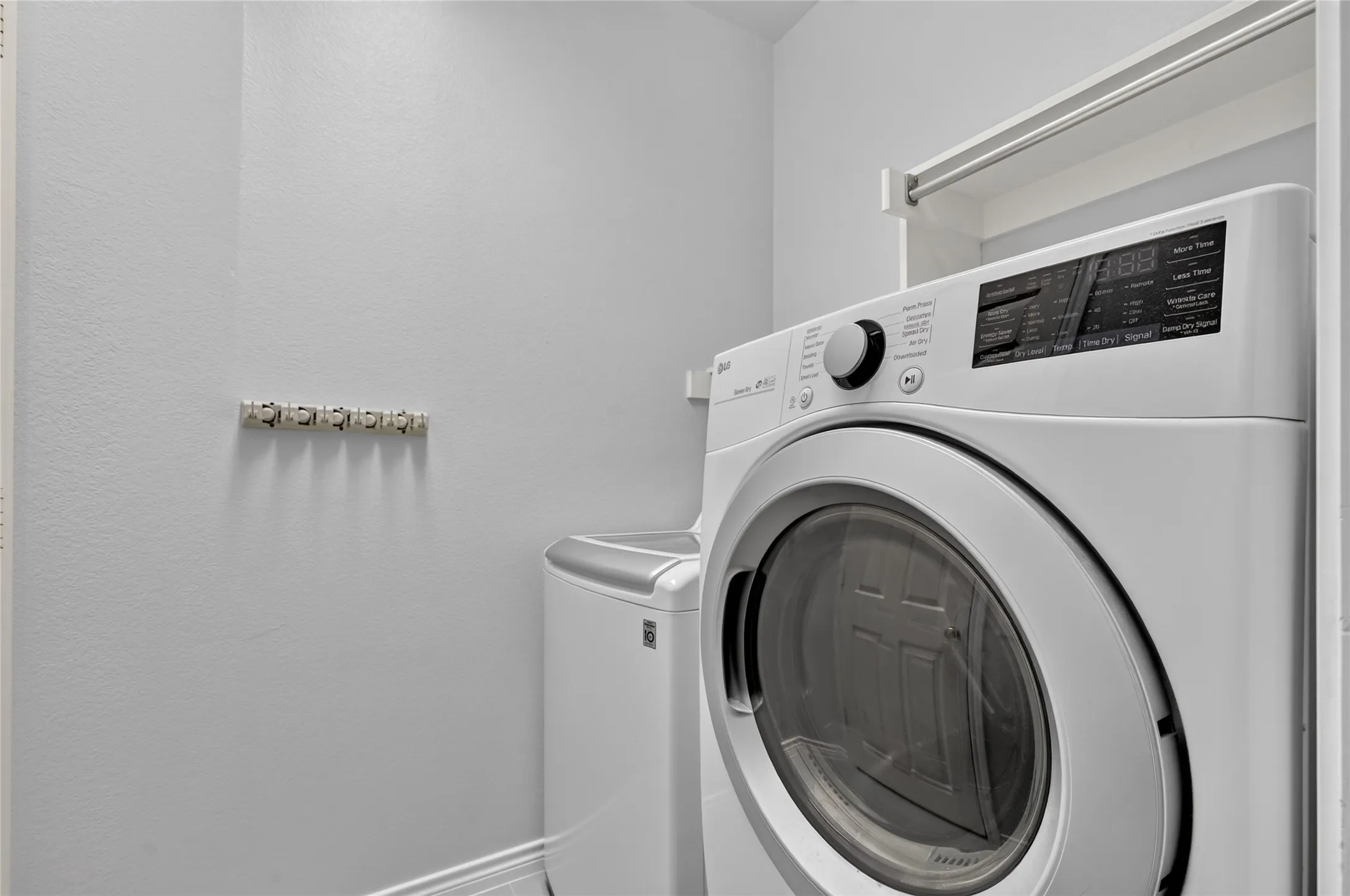 Built-in laundry appliances with a front-load dryer and top-load washer, accompanied by a wall-mounted drying rack and upper shelving for storage