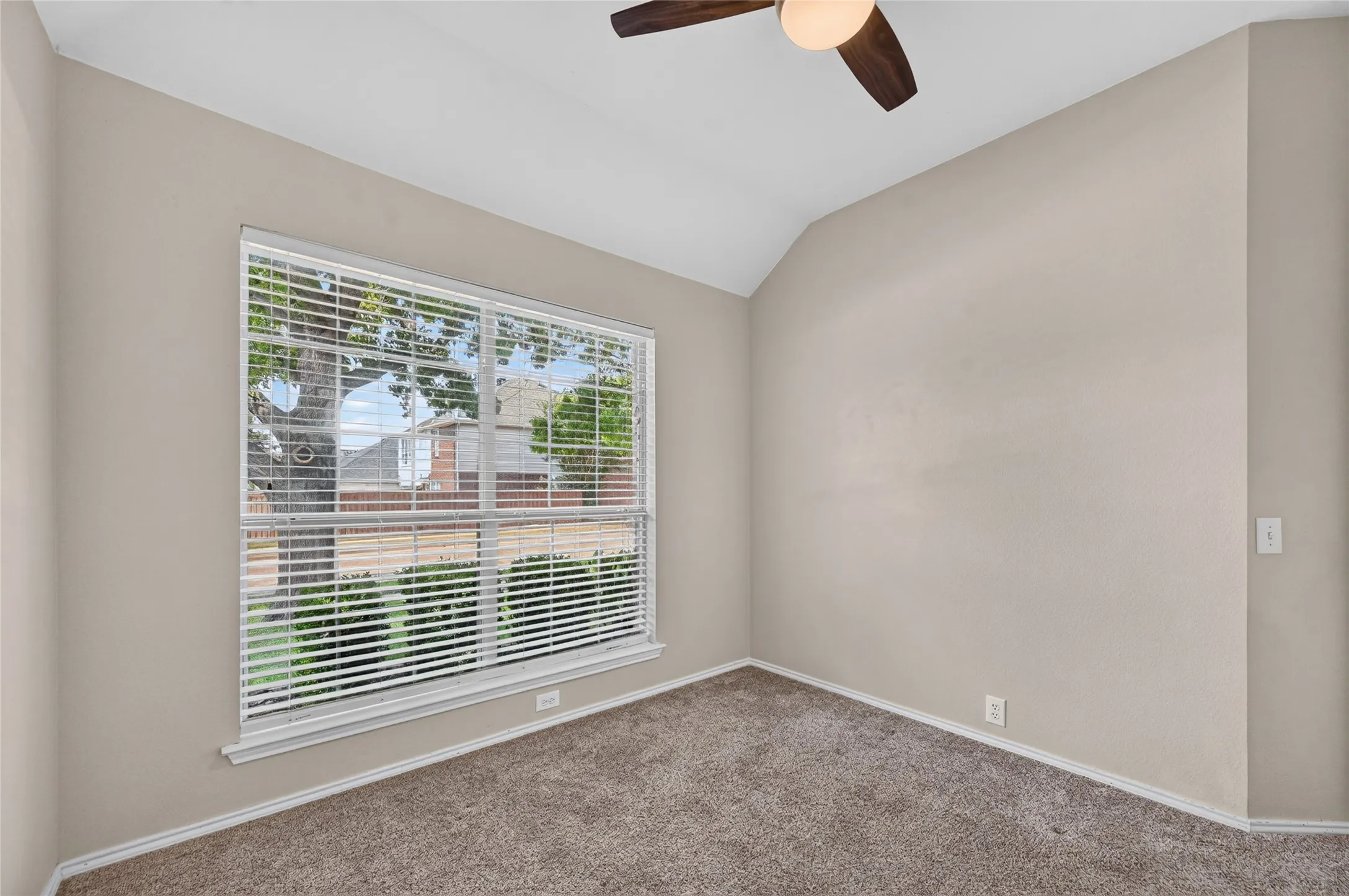 Vaulted ceiling with a ceiling fan, neutral wall paint, large window with blinds, and carpet flooring