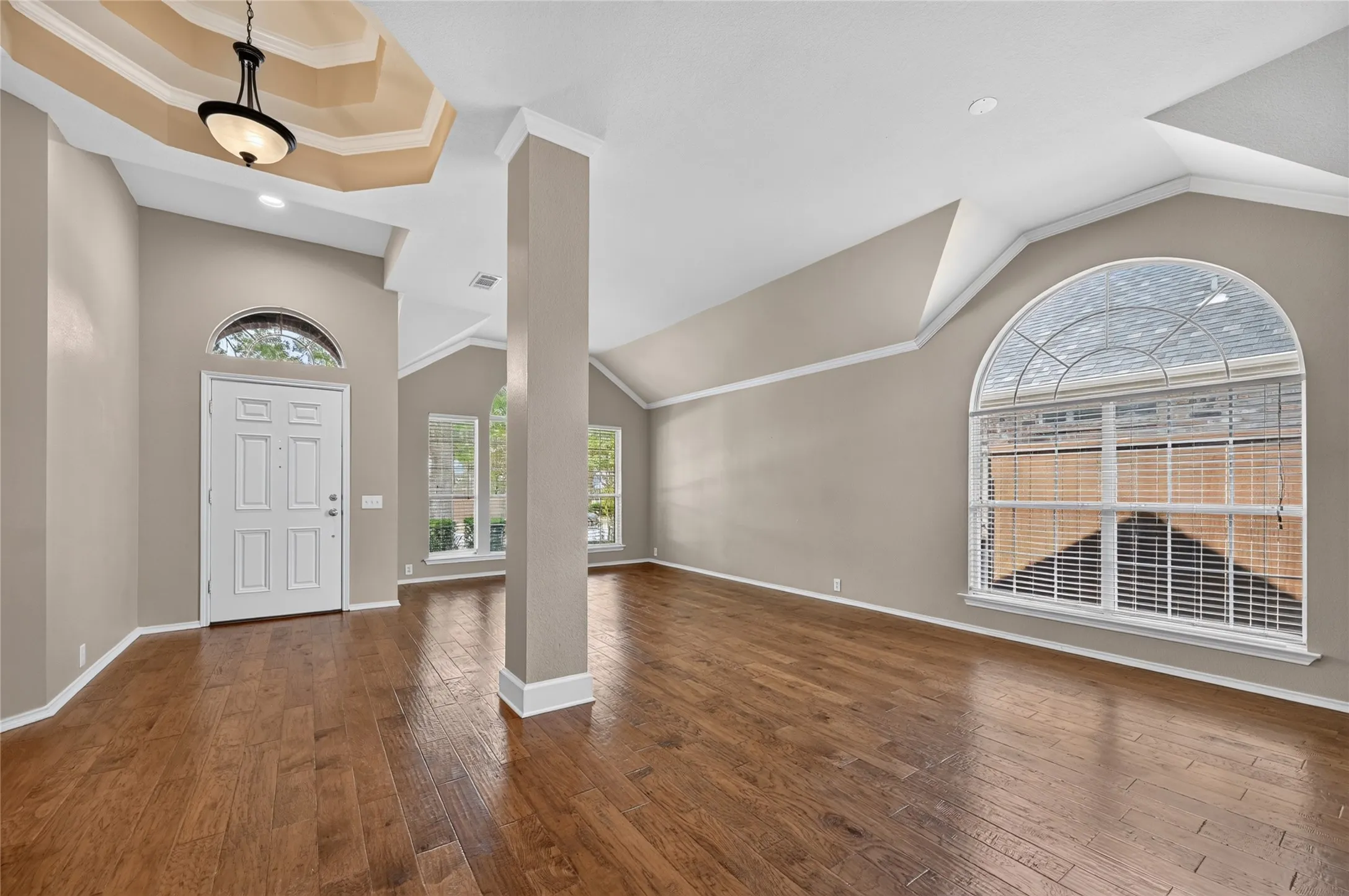 Wood-finish flooring, vaulted ceilings, tray ceiling with pendant lighting, large arched window, and recessed lighting