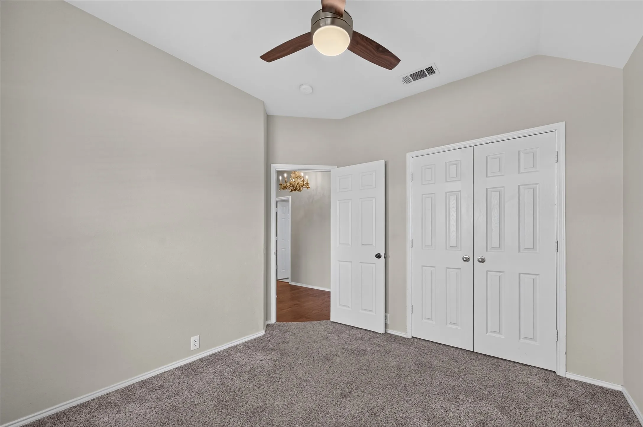 Vaulted ceiling featuring a ceiling fan with integrated lighting, neutral wall paint, and gray carpet flooring