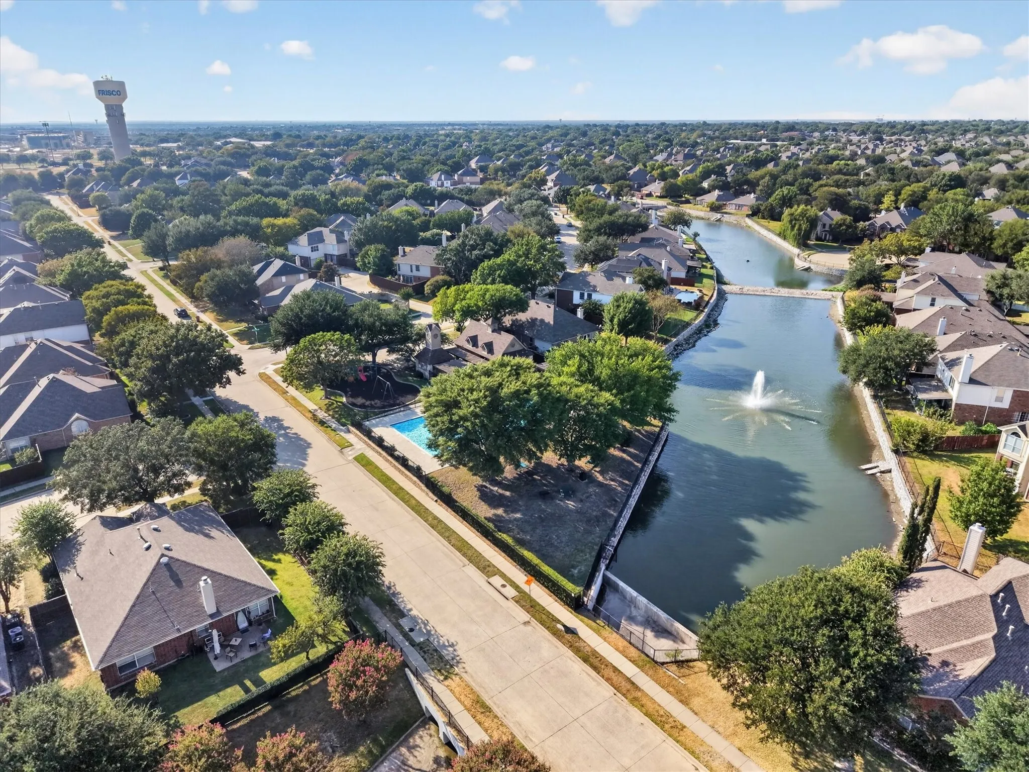 Expansive residential area featuring numerous mature trees, a waterway with a fountain, and properties with private swimming pools