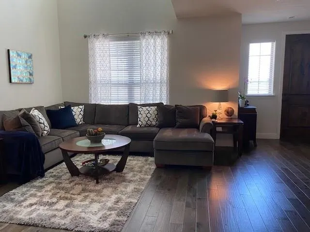 Vaulted ceiling, large window with blinds, dark wood-finish flooring, and a dark wood door