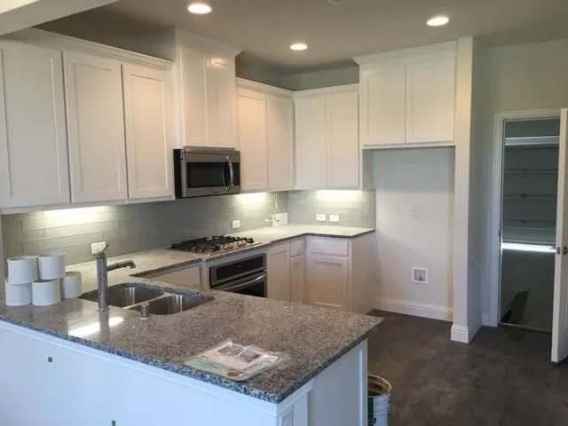 Modern kitchen featuring white cabinetry, granite-style countertops, stainless steel appliances including a gas cooktop and built-in microwave, recessed lighting, and a spacious island with seating